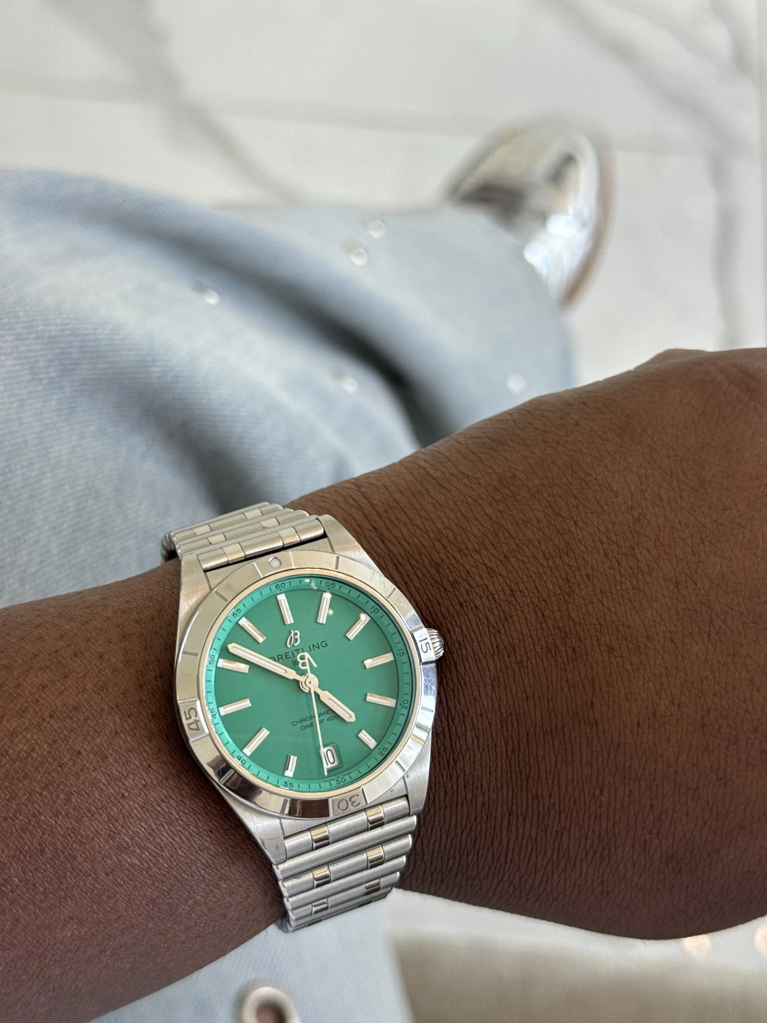 A person's wrist wearing a Breitling wristwatch with a turquoise dial.