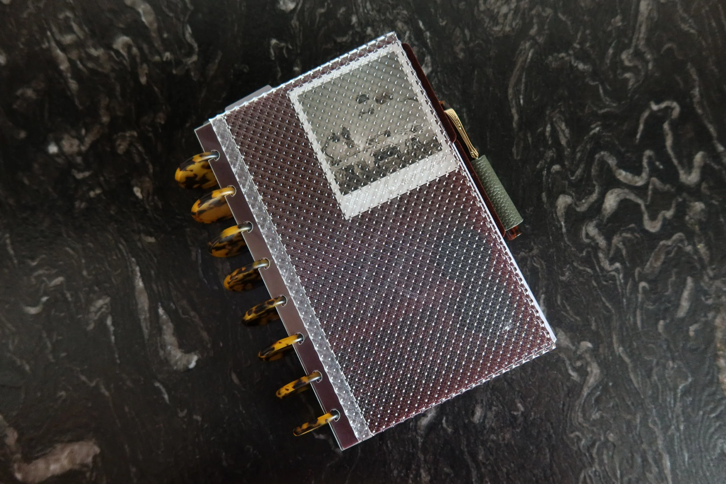 A brown and transparent spiral notebook with a textured cover, tied with a thin string, resting on a black marbled surface.
