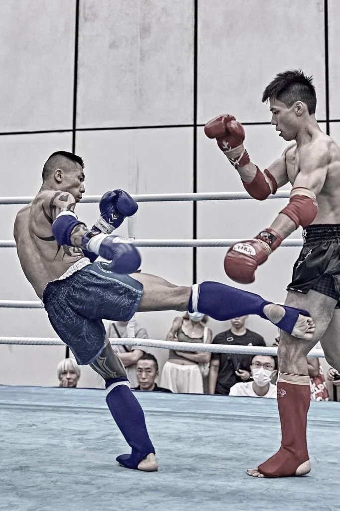 A male mixed martial arts fighter standing inside a cage with his hands by his sides, wearing black shorts, red gloves, and red shin guards, with a serious expression.