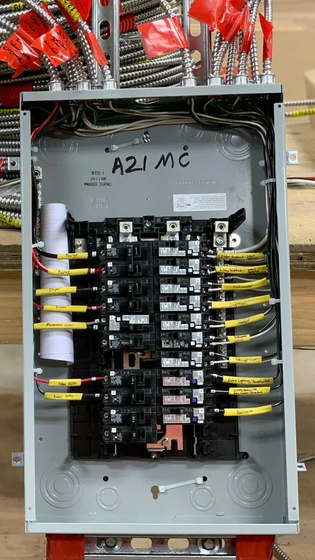 Electrical panel with various wires and yellow labels indicating different circuit connections such as range, microwave, HVAC, refrigerator, and dishwasher.