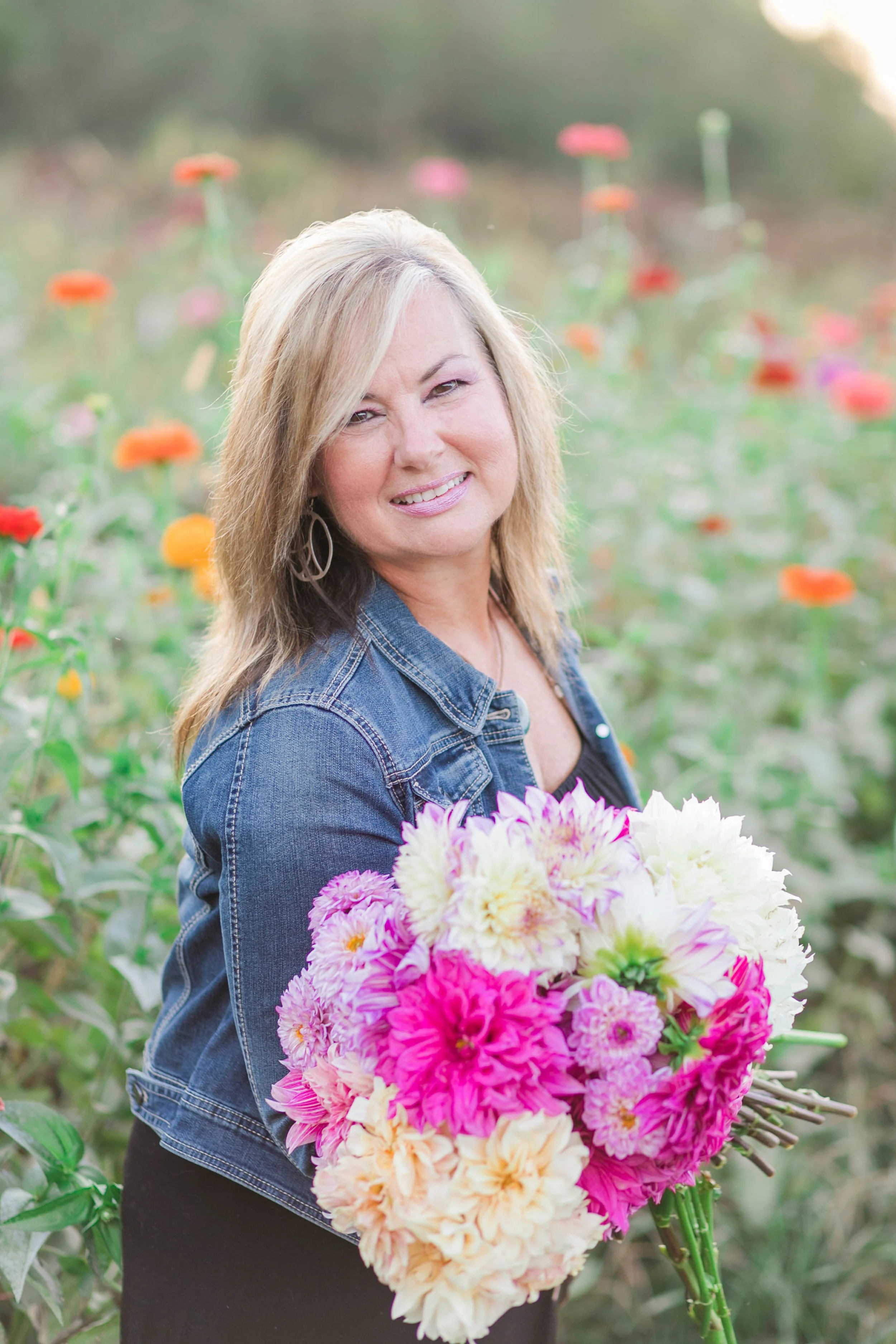 Cindy Thomas, owner of The Reserve at Two Horses Farm, standing in a manicured flower field holding a bouquet of garden blooms