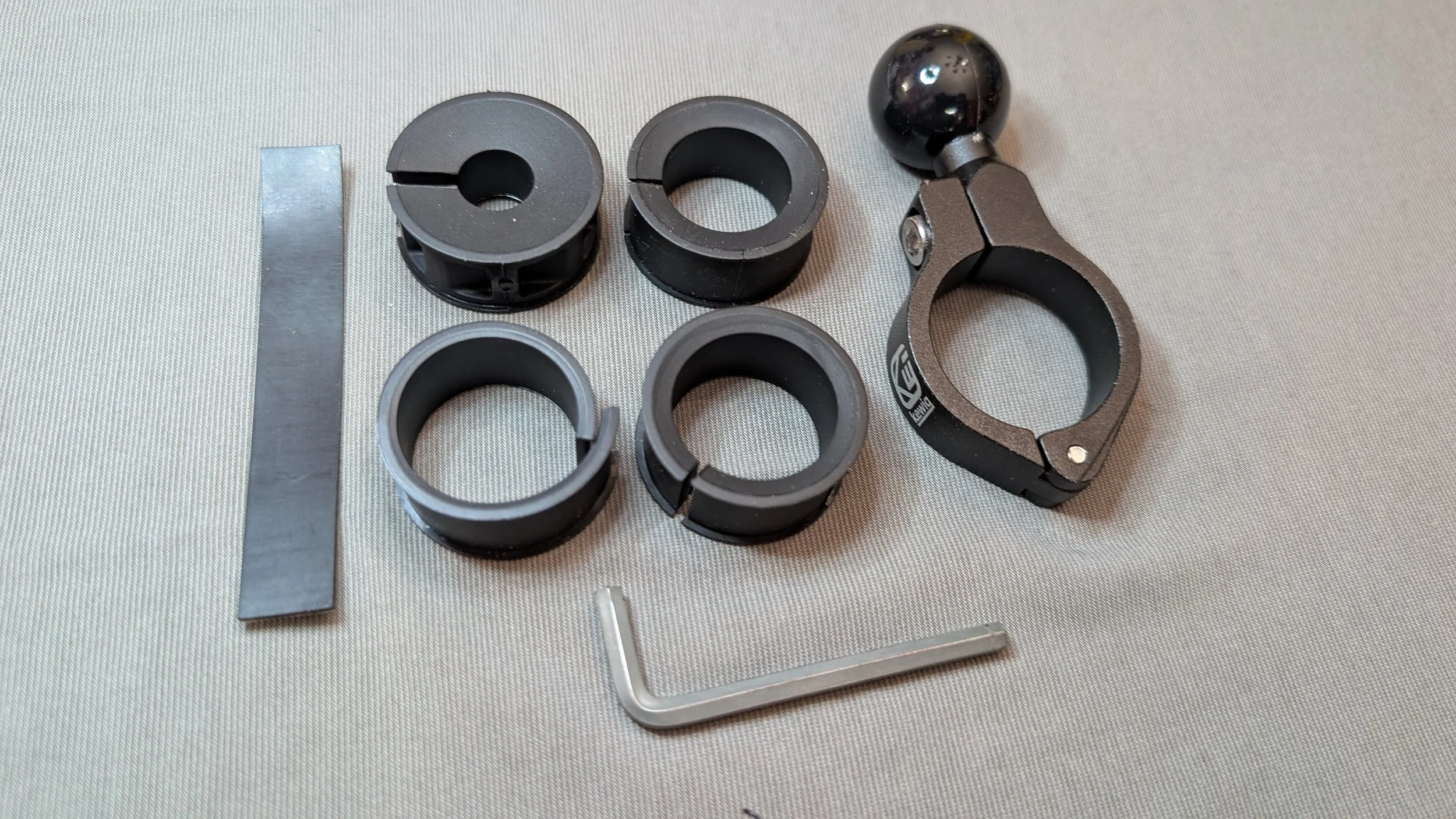 Various black and gray metal and plastic parts and tools on a light-colored surface, including ring components, a long thin metal strip, and small metal rods.