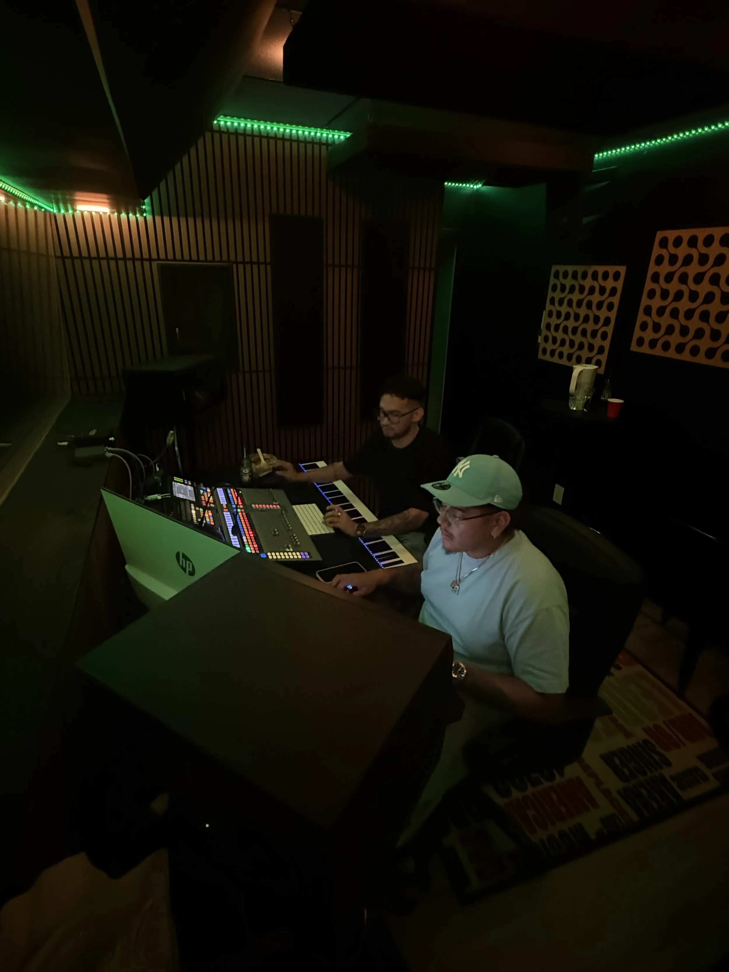 Two men working in a dark, illuminated recording studio with colorful LED lights, music equipment, and computers.