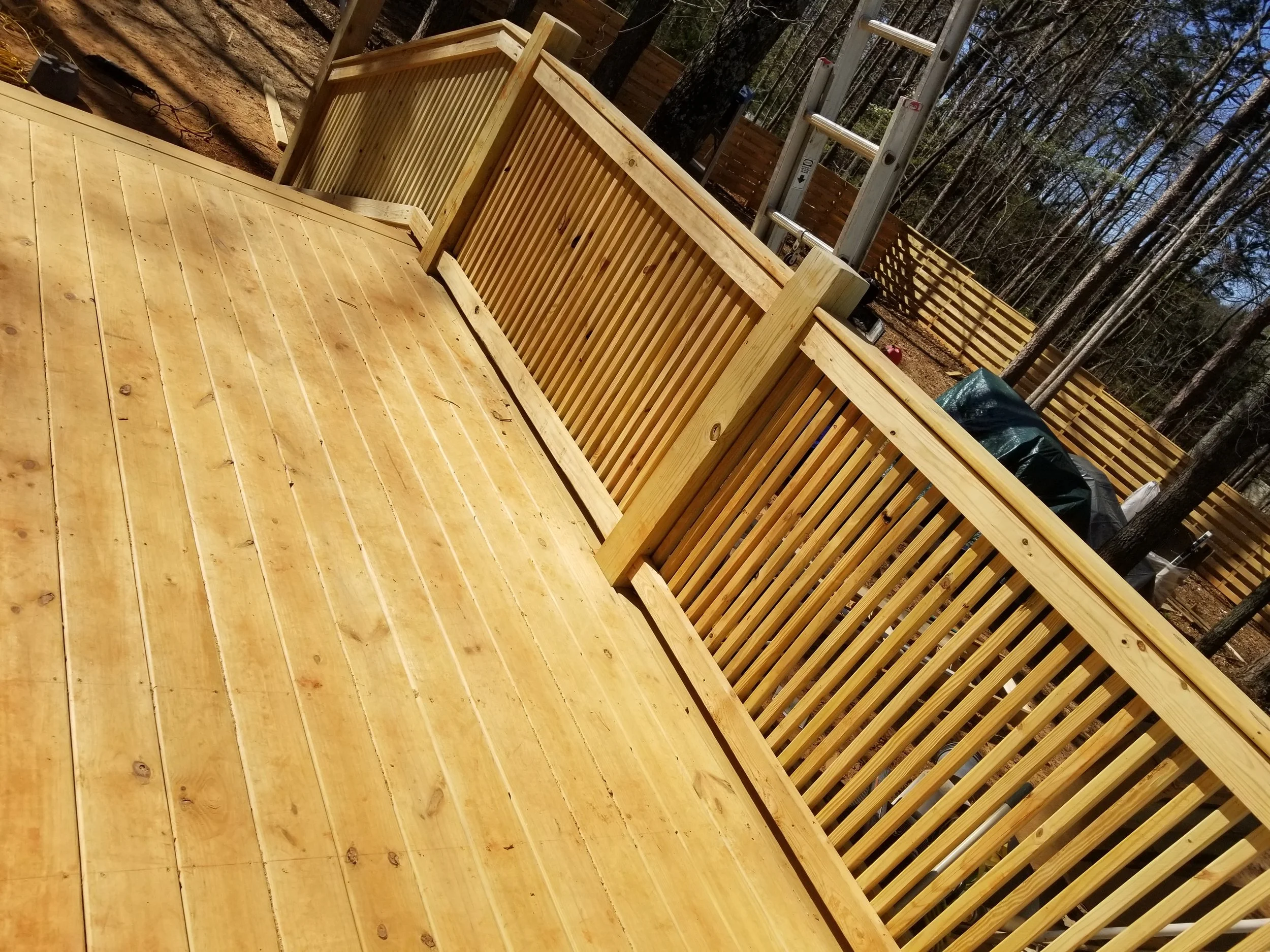 Newly built wooden deck with railing in a backyard surrounded by trees.