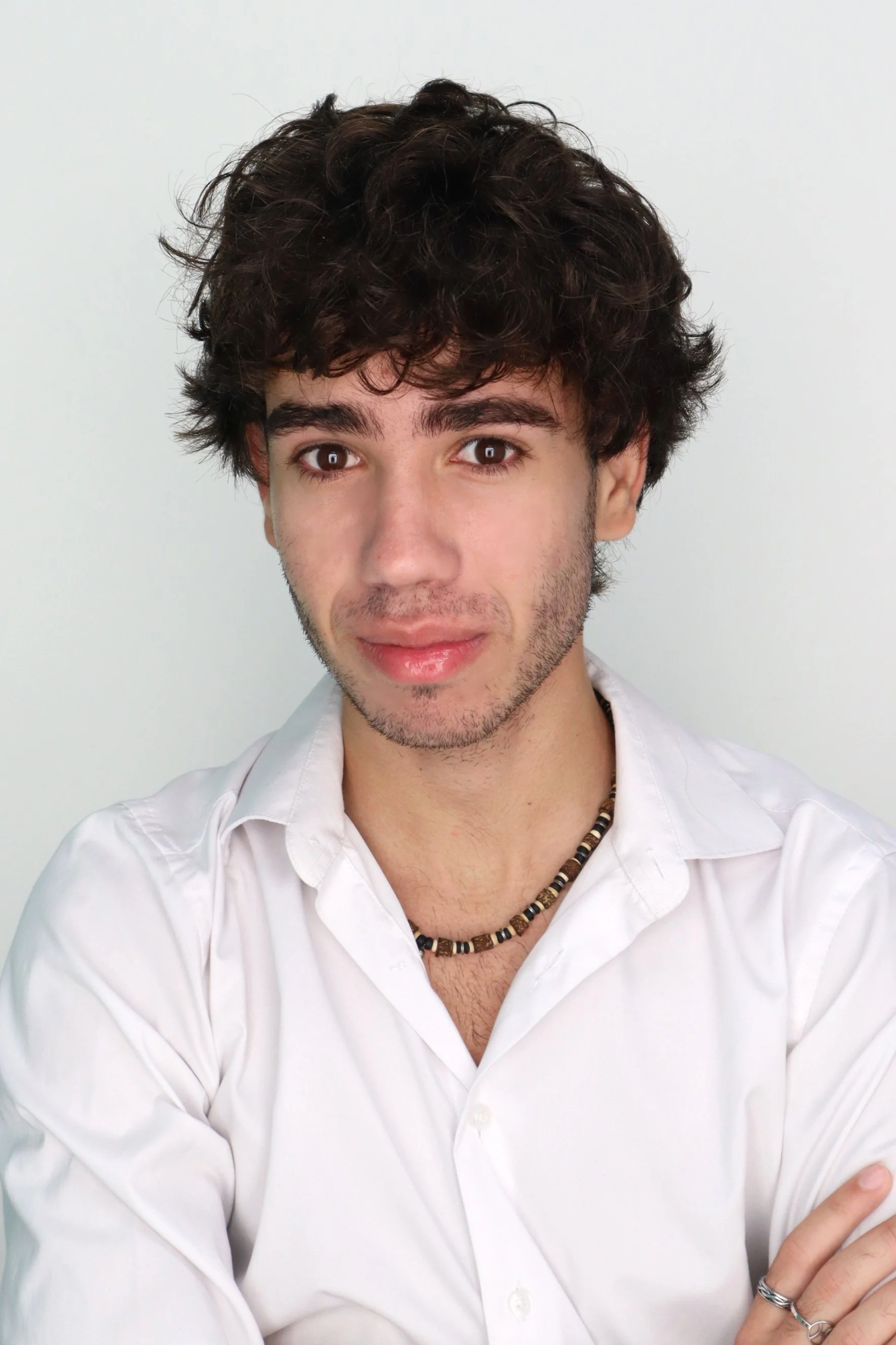 A man with dark curly hair, a beard, and glasses looking slightly to the side indoors with a plant and a wall in the background.