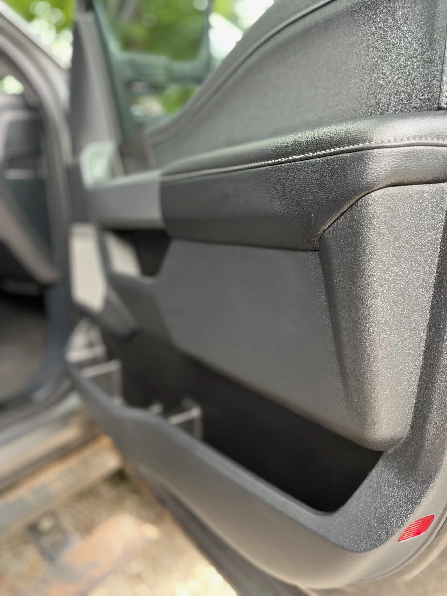 Close-up of the interior side of a car's passenger door with a storage compartment and a red reflector.