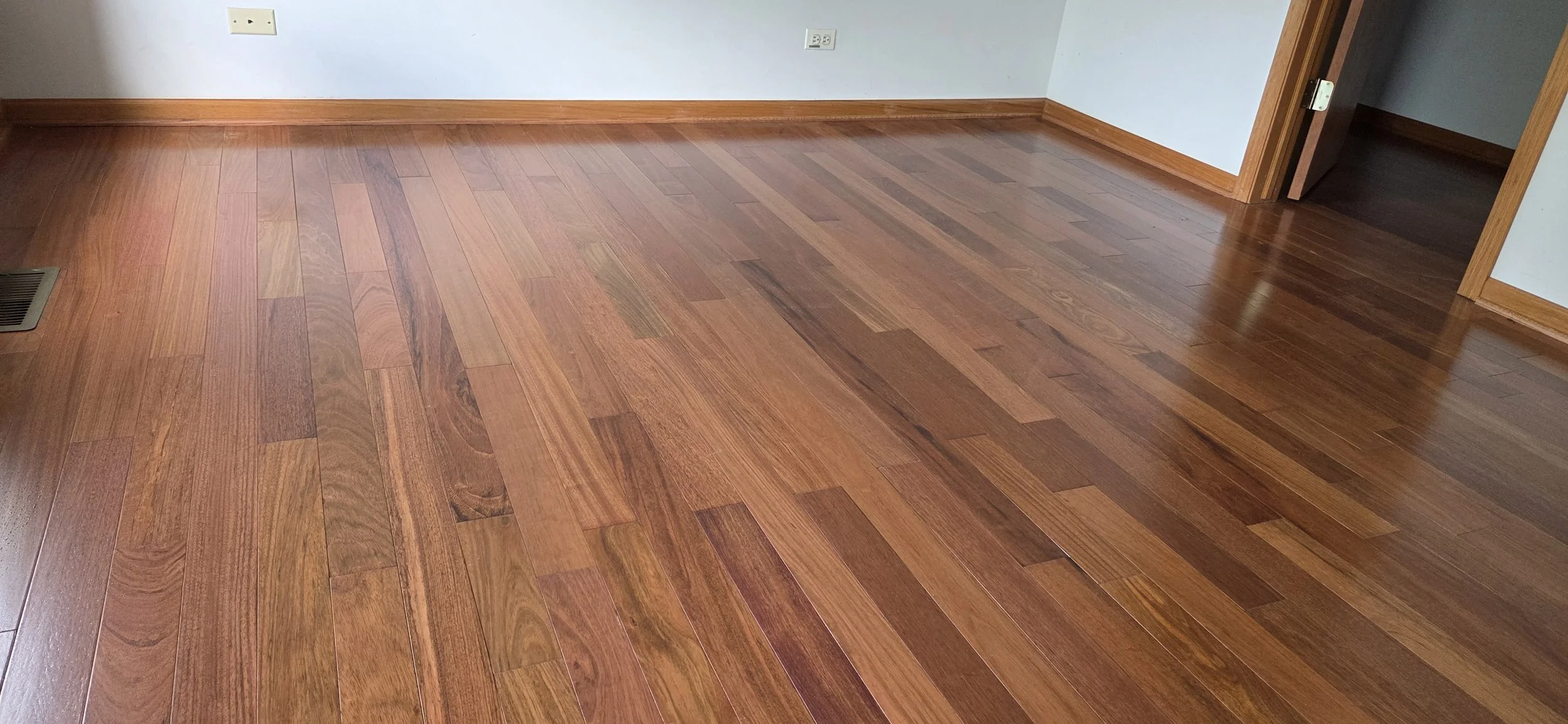 Empty room with wooden floors, white walls, electrical outlets, and a doorway.