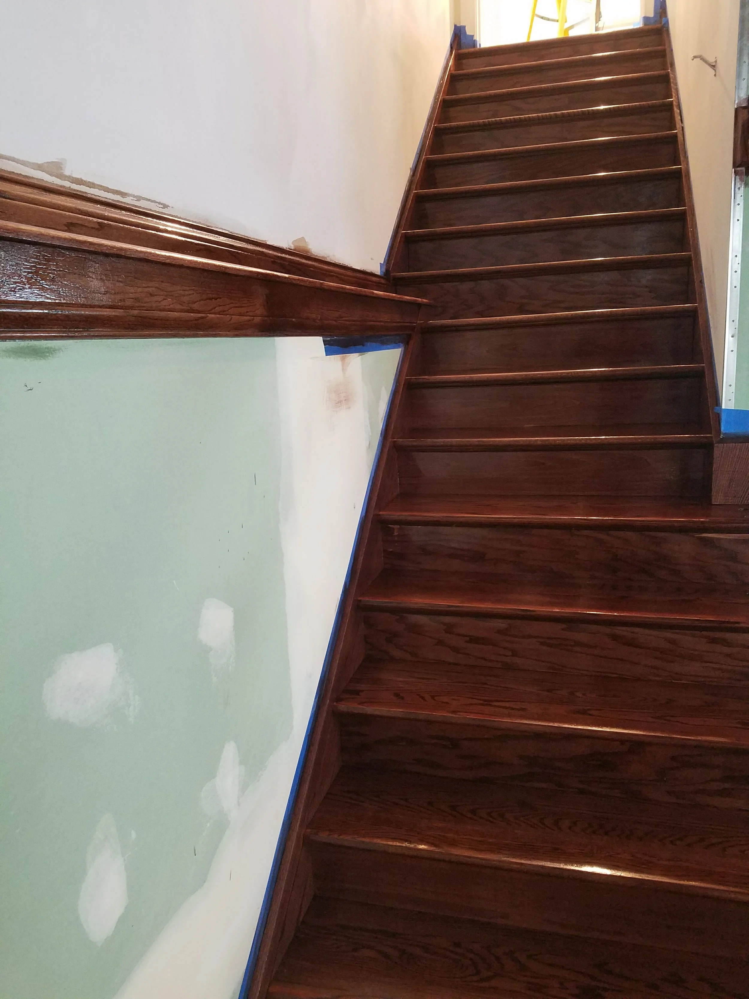 Wood stairs and a green wall with patches of white paint and blue painter's tape.