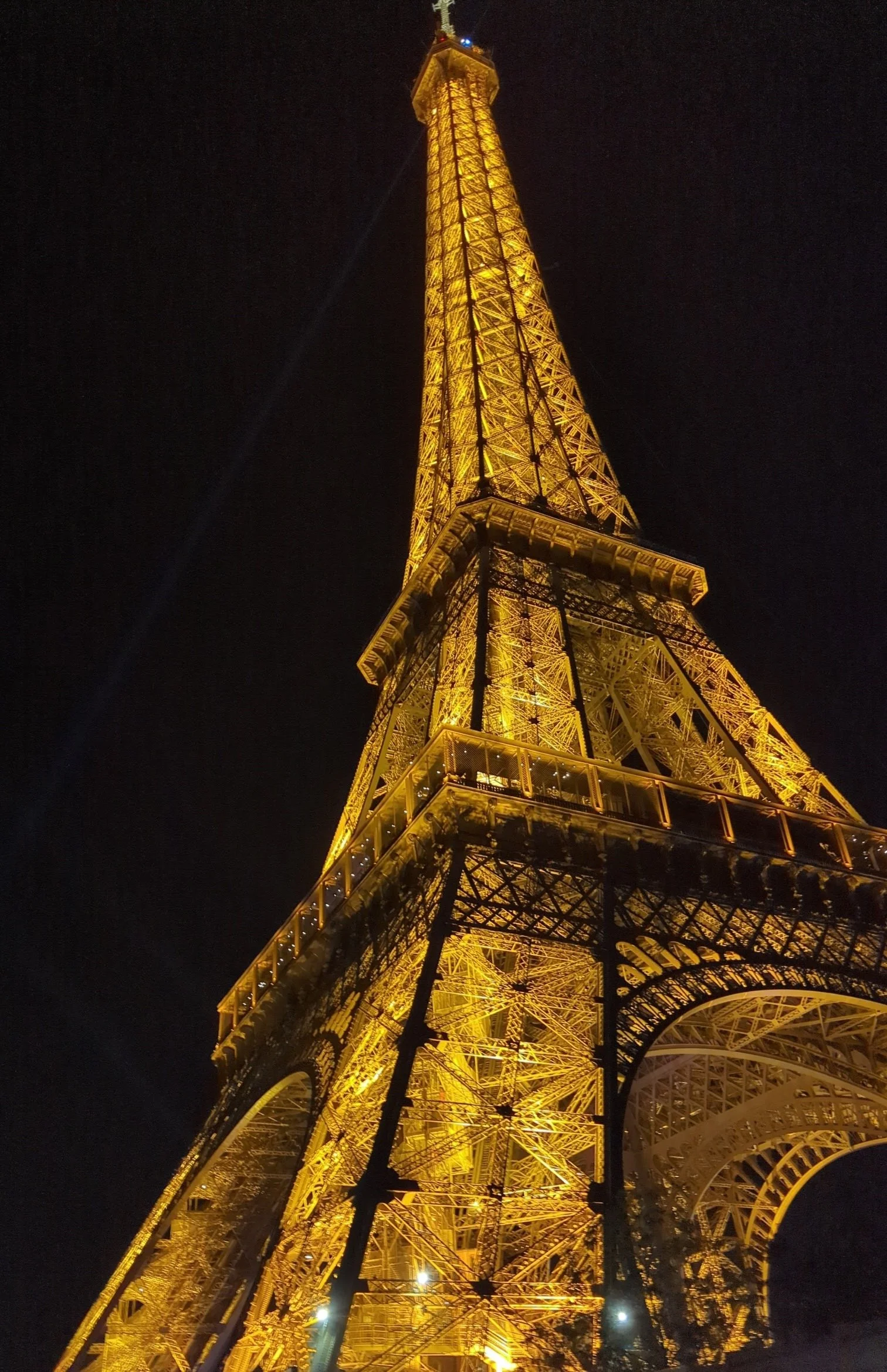 The Eiffel Tower illuminated with yellow lights at night, viewed from below.