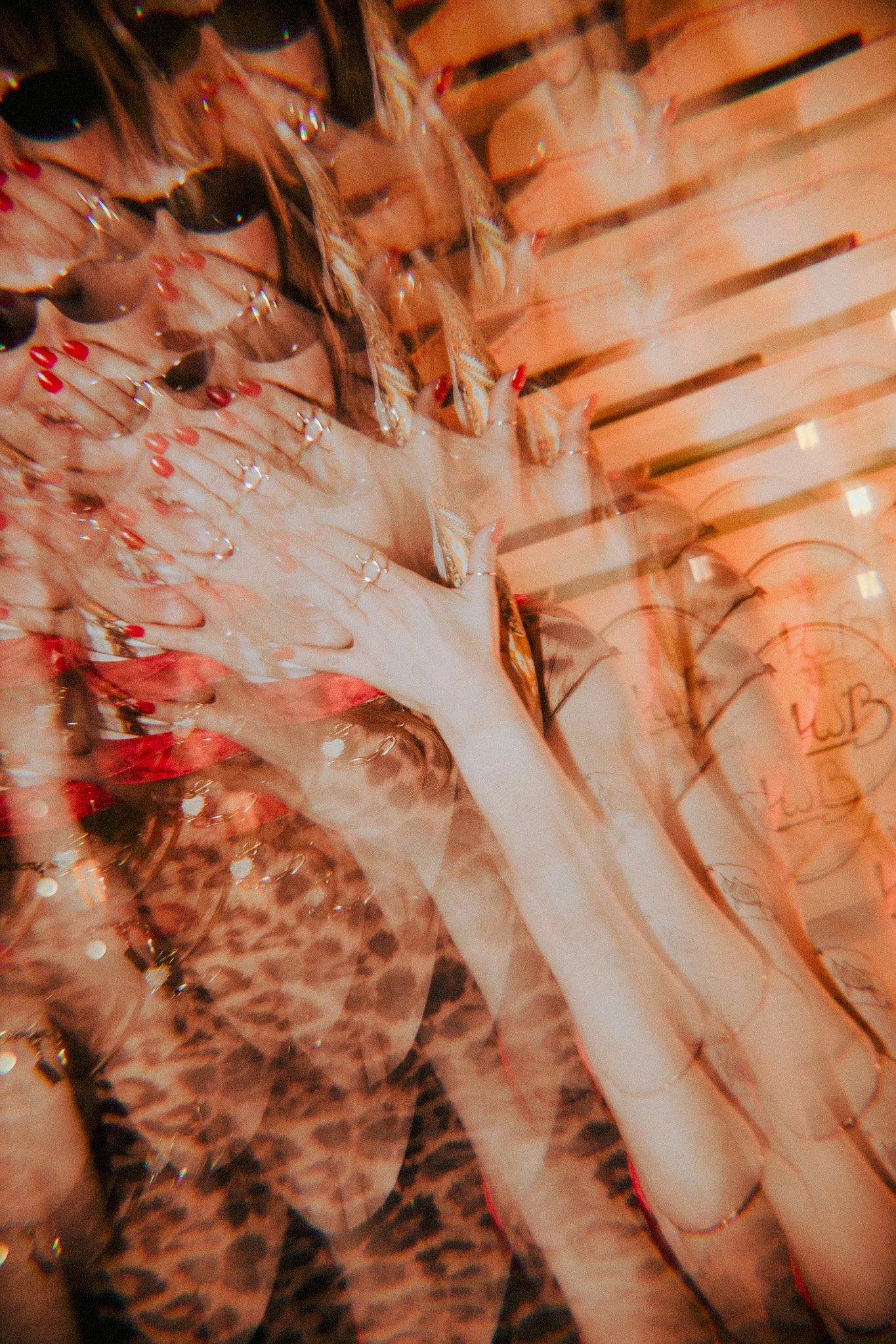 A person with red nail polish and rings on their fingers is holding a pair of shoes with feather details, standing in front of a backdrop of orange paper bags with writing on them.