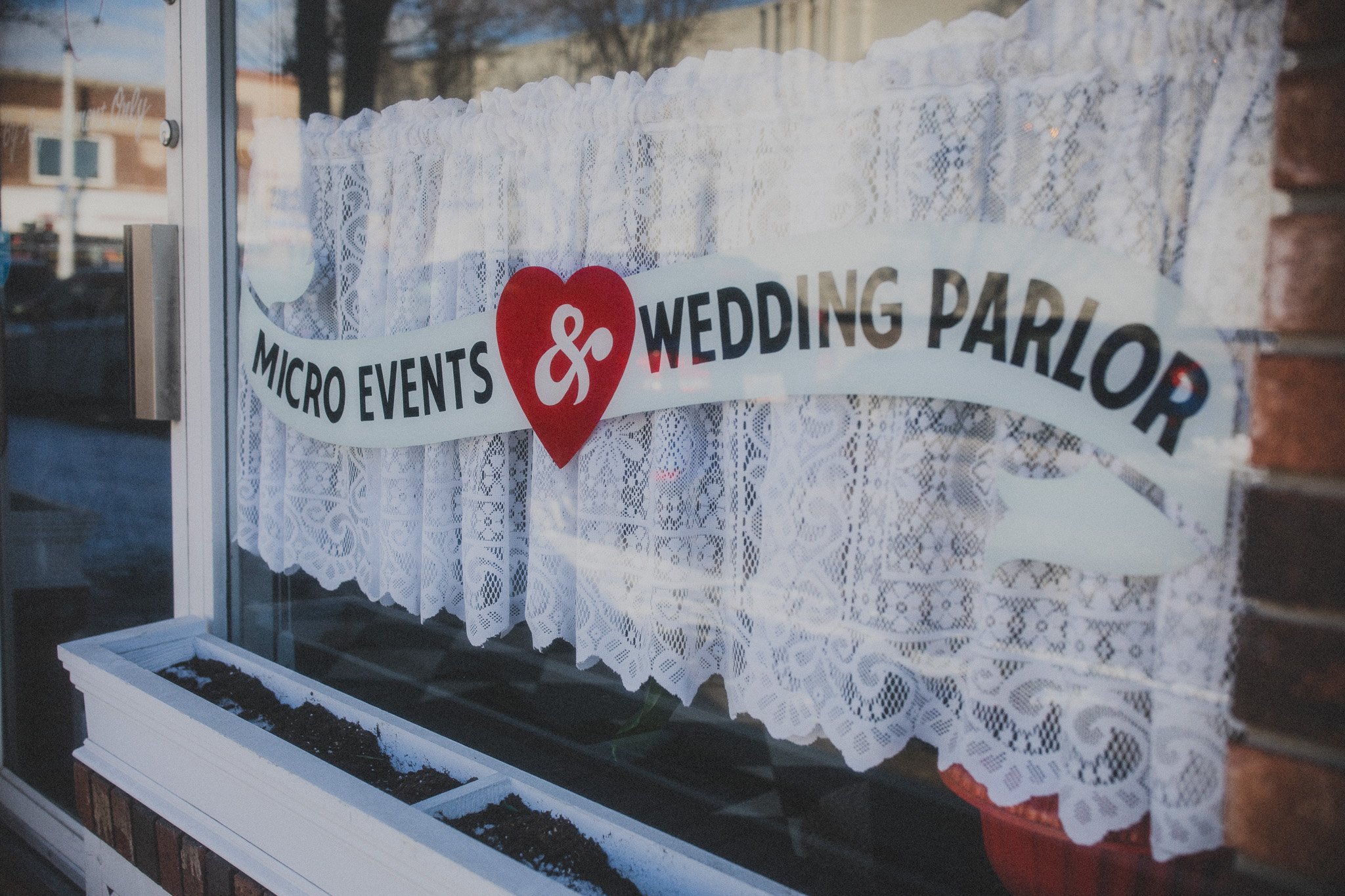 Storefront window with lace curtains and Shop sign reading 'Micro Events & Wedding Parlor' with a red heart in the center.