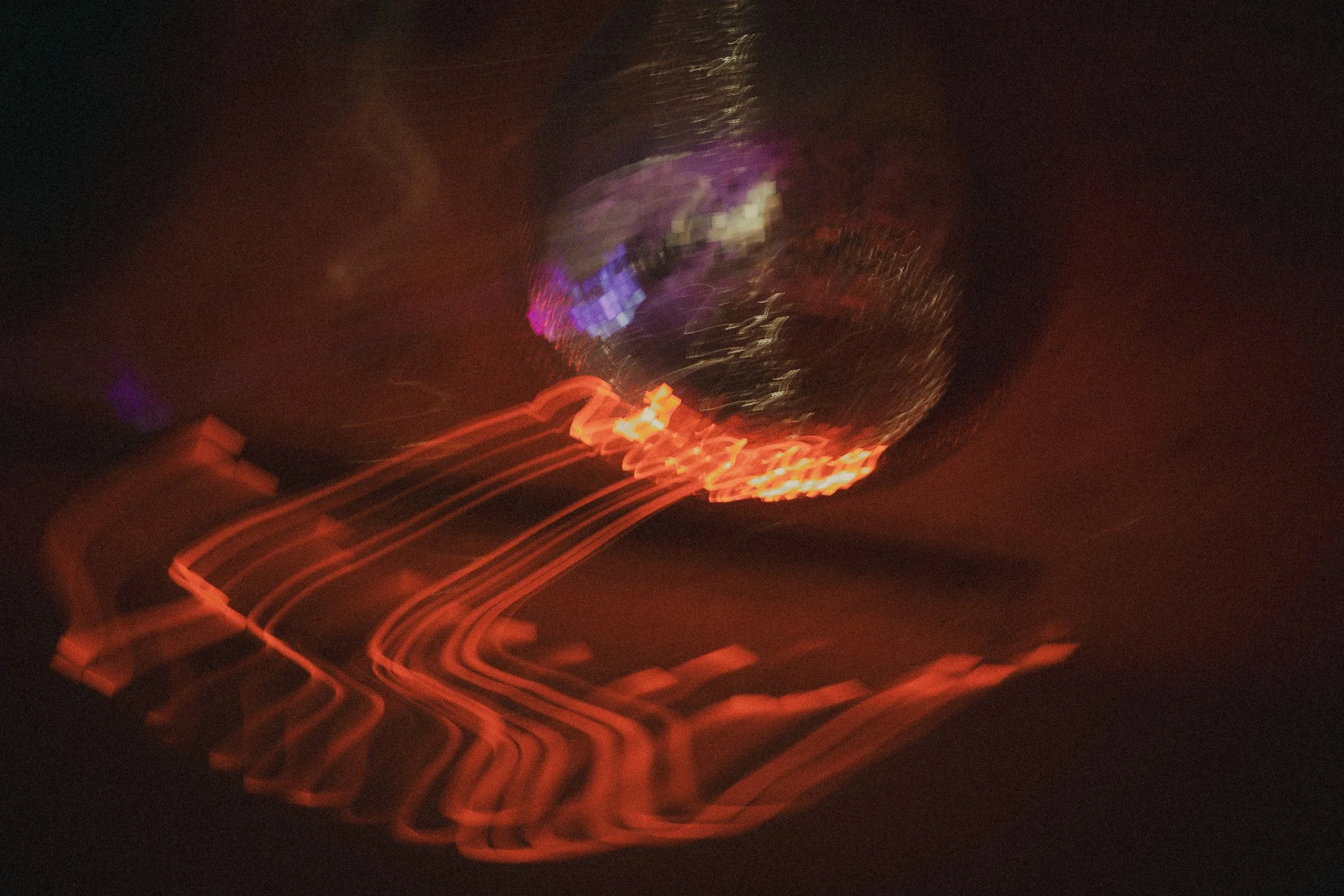 Long exposure photo of a brightly lit sign with red neon lights creating swirling lines and a reflective shiny surface, possibly a globe or spherical object.