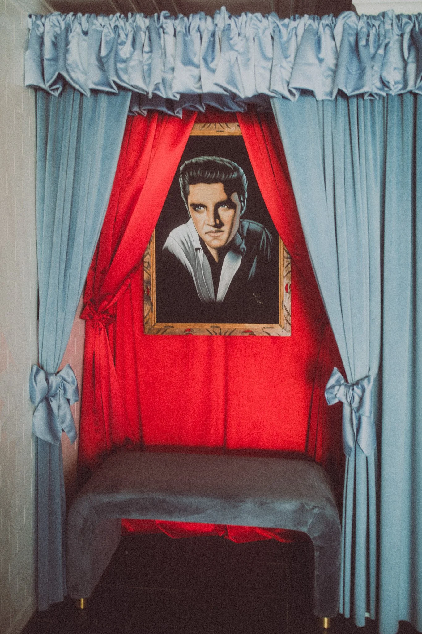 A portrait of Elvis Presley displayed in a red and blue curtain setup, with a velvet bench in front.