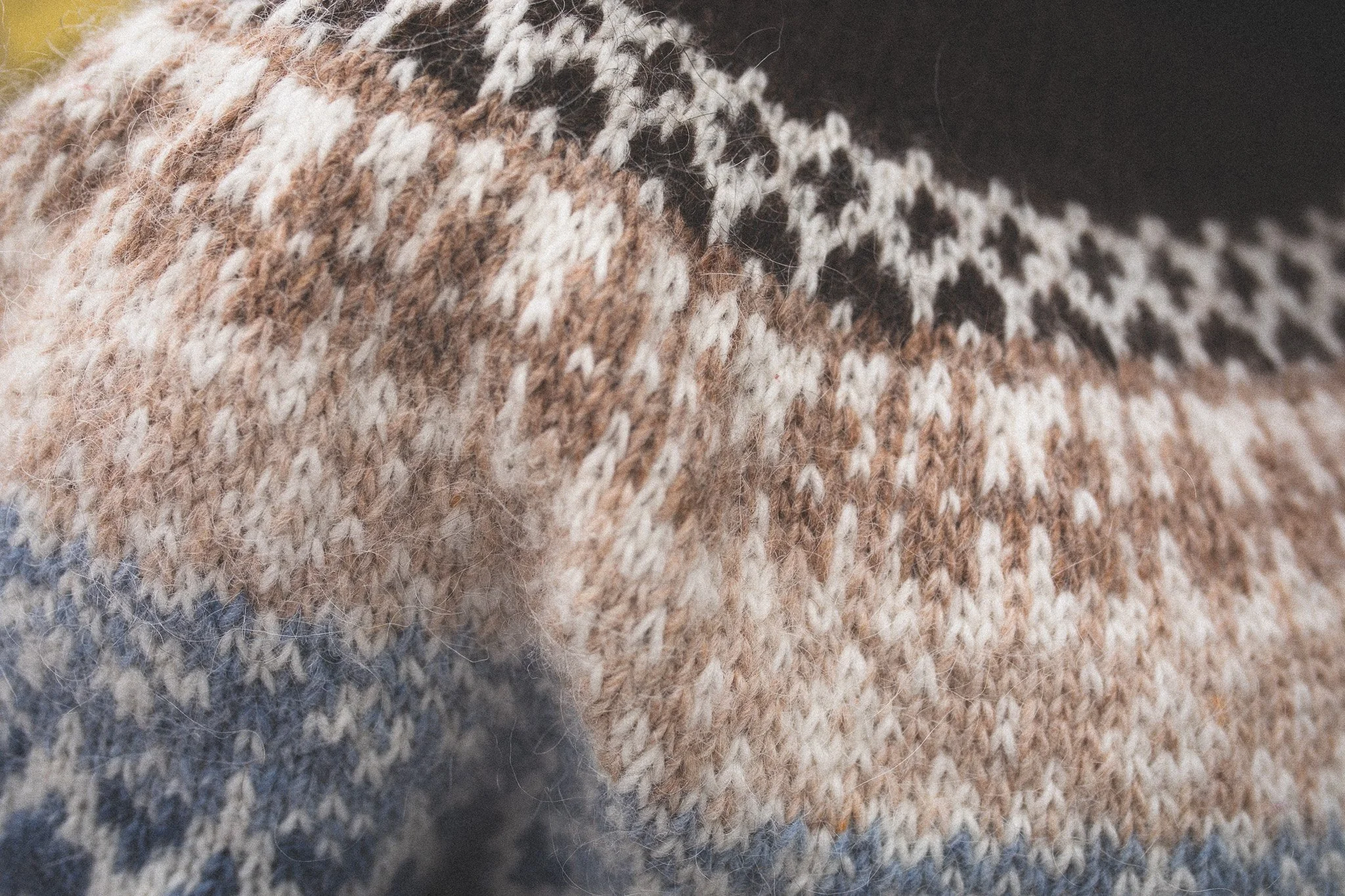 Close-up of a multicolored knit sweater featuring a pattern of black, white, brown, and beige yarns.