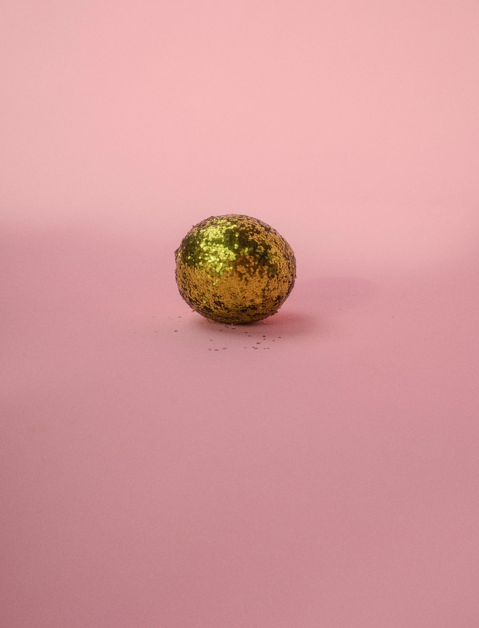 A glittery gold spherical object on a pink background.
