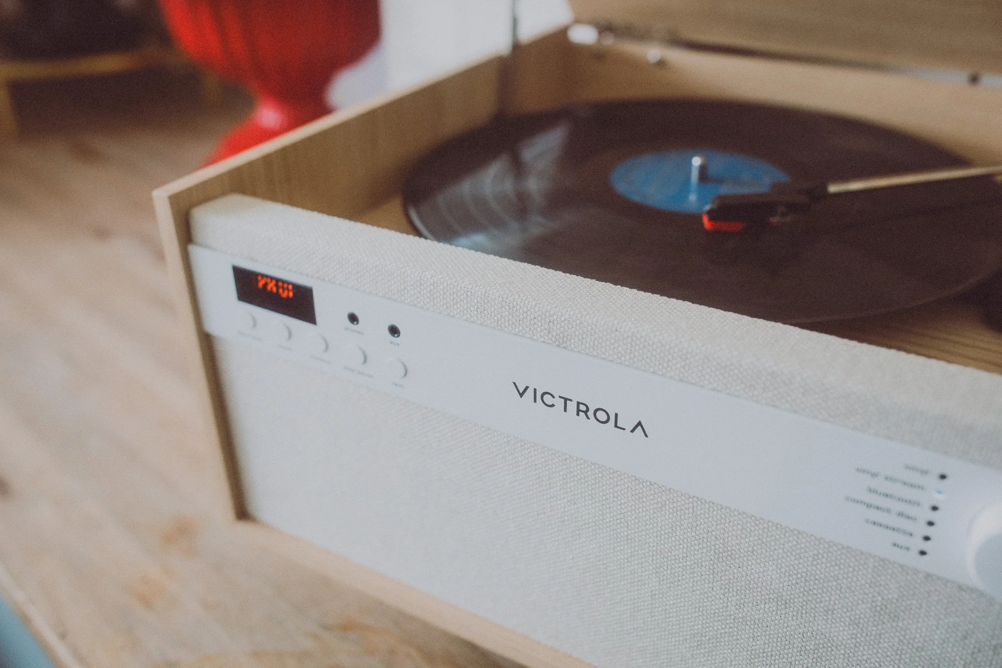 A white Victrola record player with selected buttons on the front, playing a vinyl record, in a wooden box.