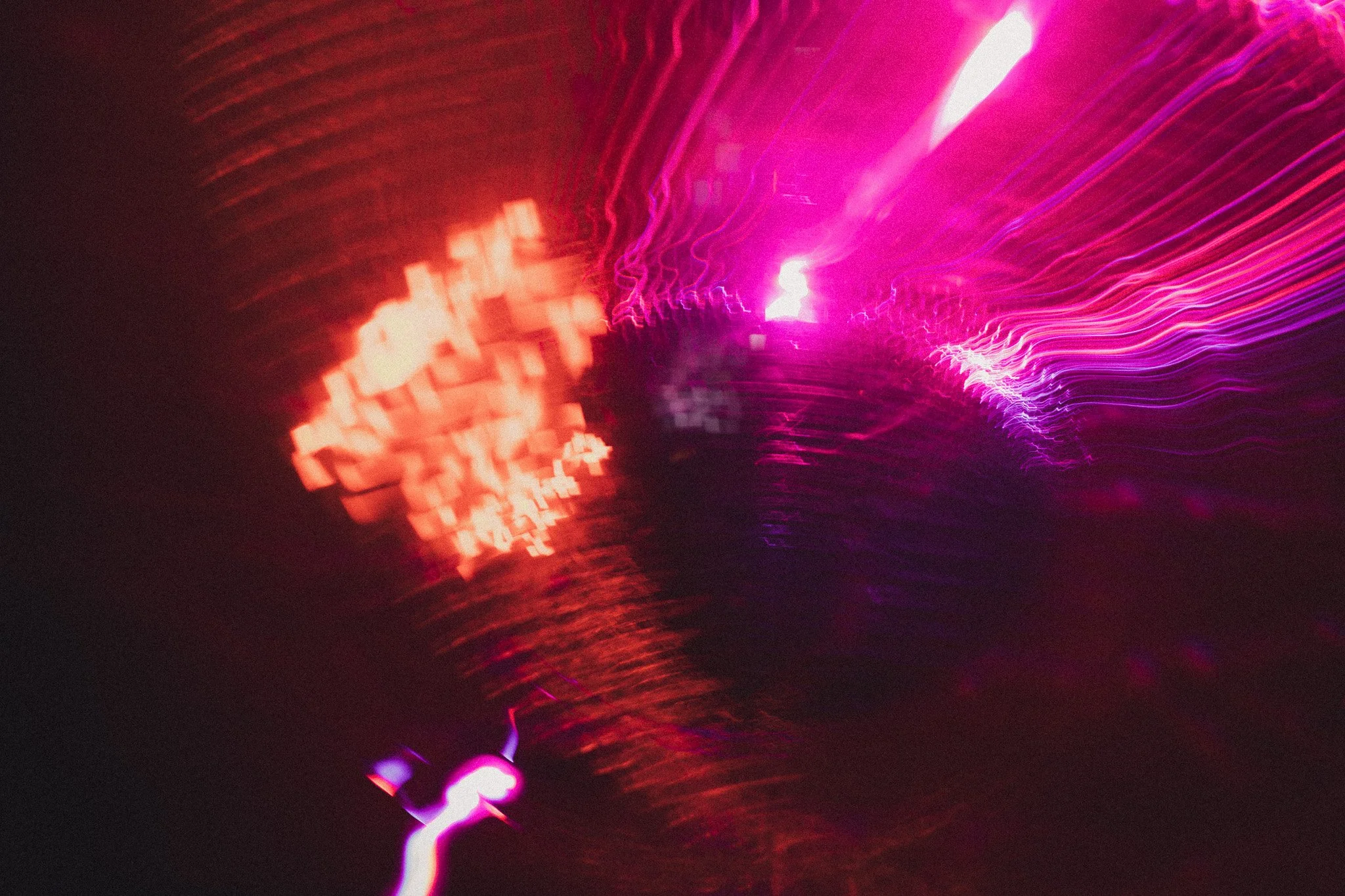 Abstract photo of colorful light streaks in pink, purple, and red hues on a dark background.