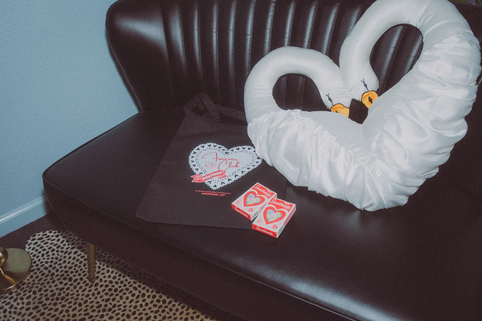 A black leather bench with a white swan-shaped pillow, Valentine's Day cards, and heart-themed decorations on a black cloth.