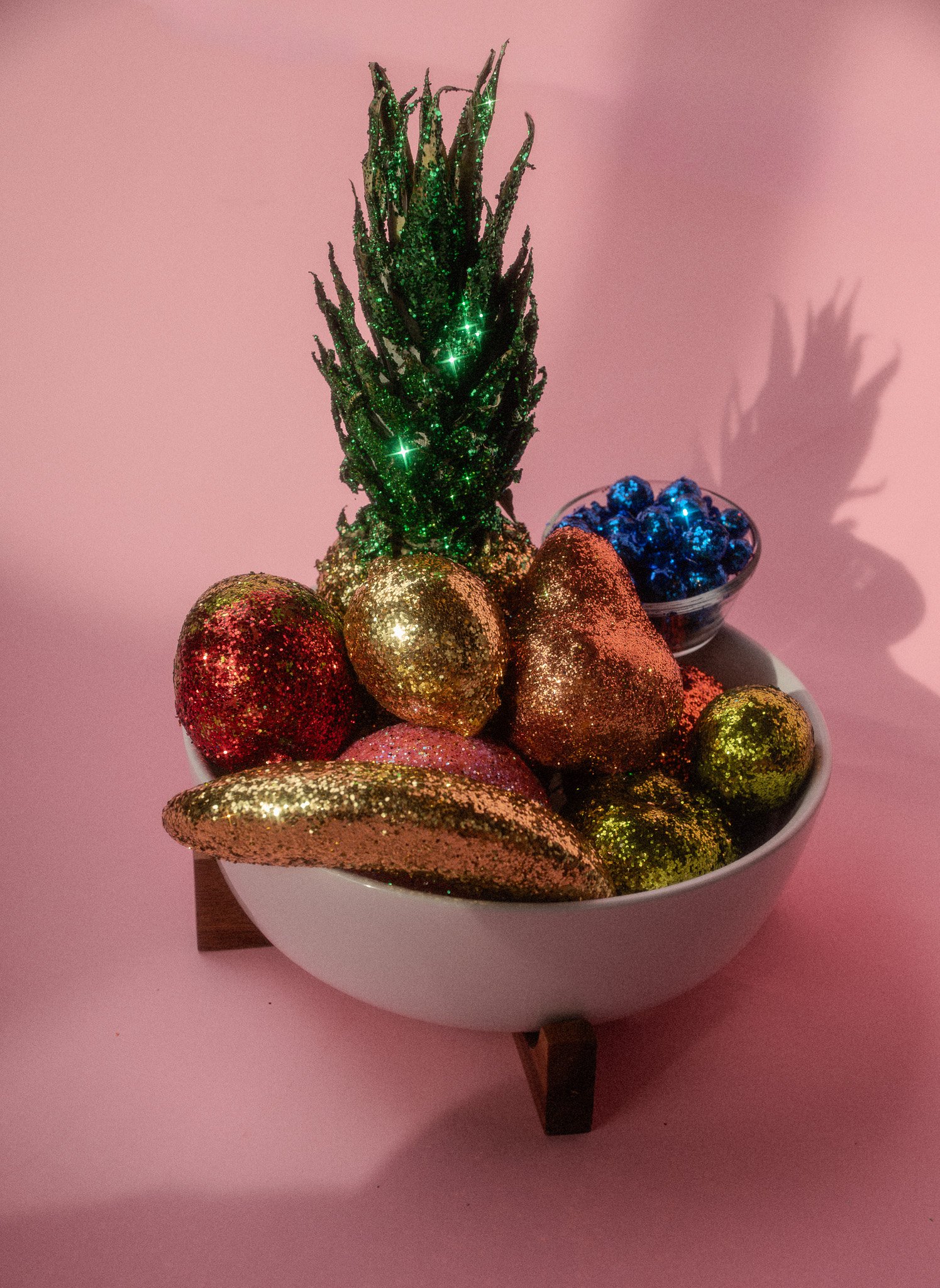Decorative bowl with glittery Christmas ornaments, including a small glittery Christmas tree, in front of a pink background.