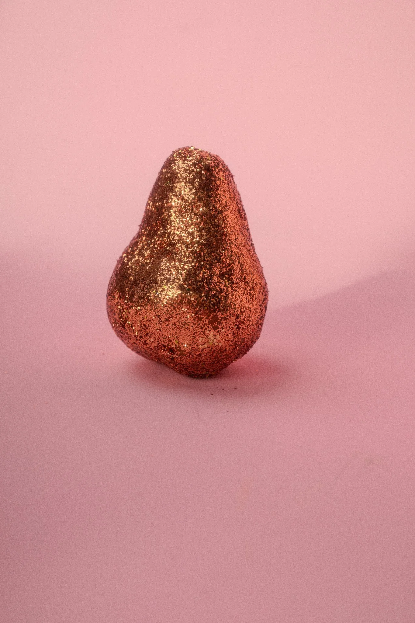 A pear-shaped object covered in gold glitter, placed on a pink background.
