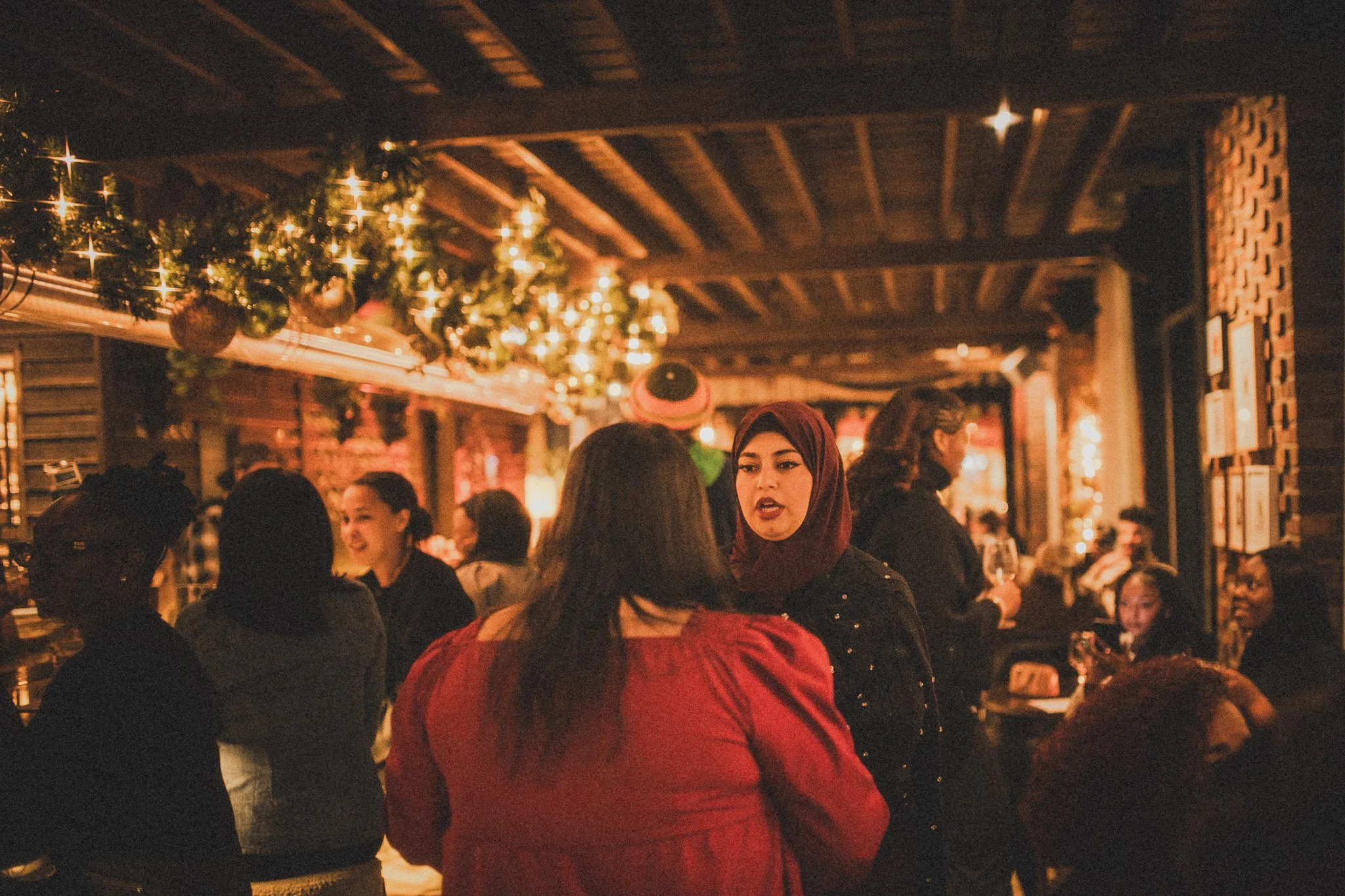 People socializing in a warmly lit, festive restaurant decorated with Christmas ornaments and string lights.