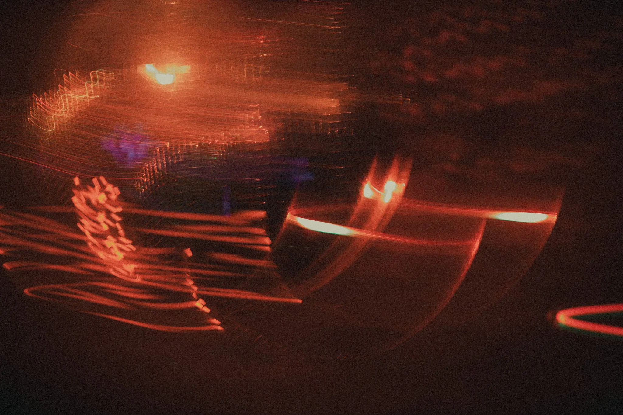Abstract image with streaks of red, orange, and purple light against a dark background, creating a sense of motion and light trails.