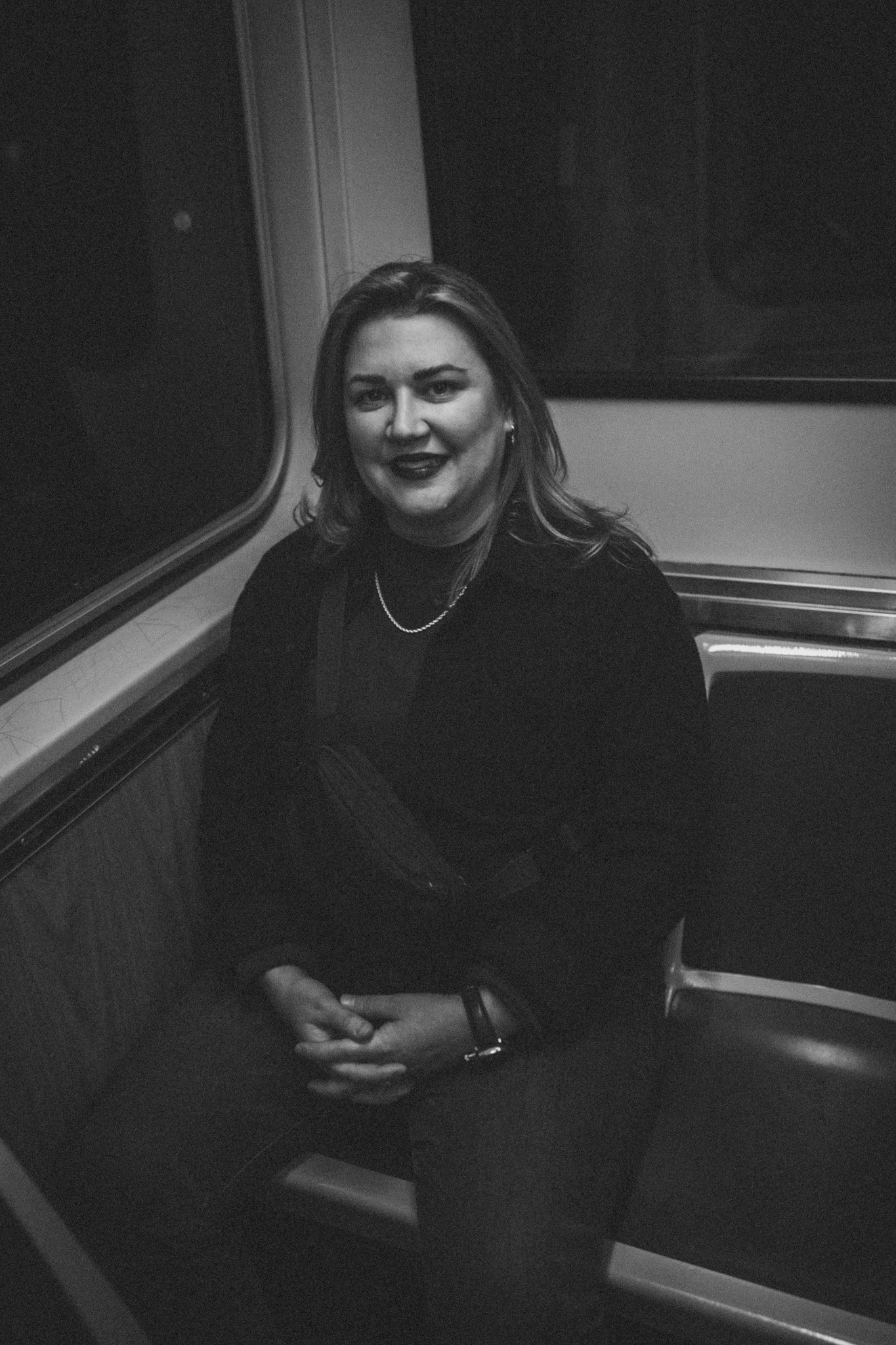 A woman with shoulder-length hair and dark lipstick sitting on a train.