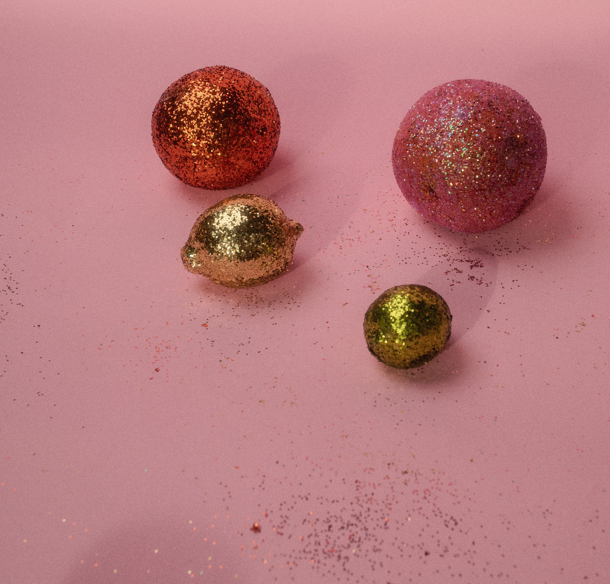 Decorative glitter-covered fruit-shaped ornaments on a pink background.