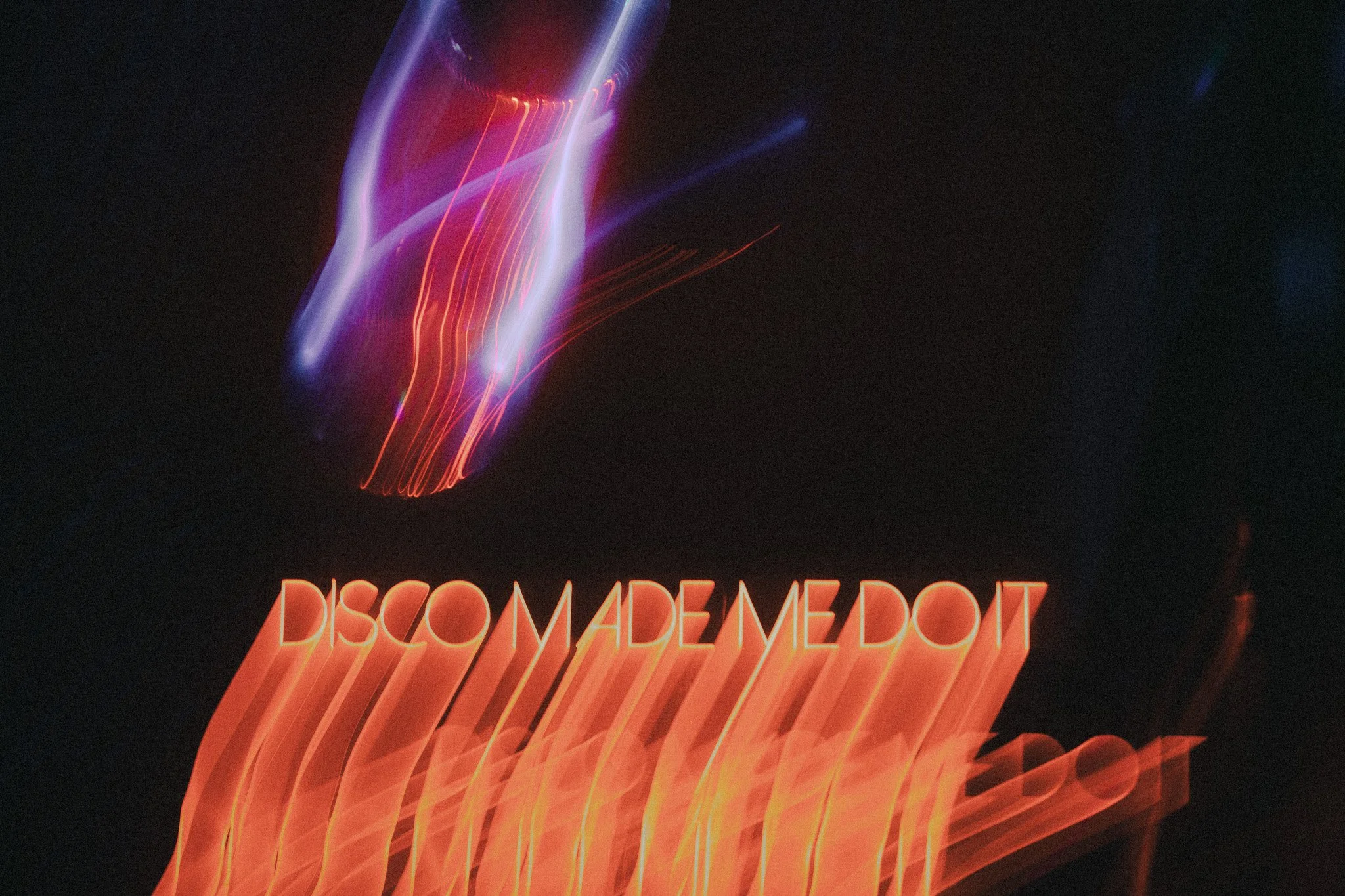 Neon sign with the words 'DISCOTAGE MEDIUM' in orange, with abstract colorful light streaks above it against a dark background.