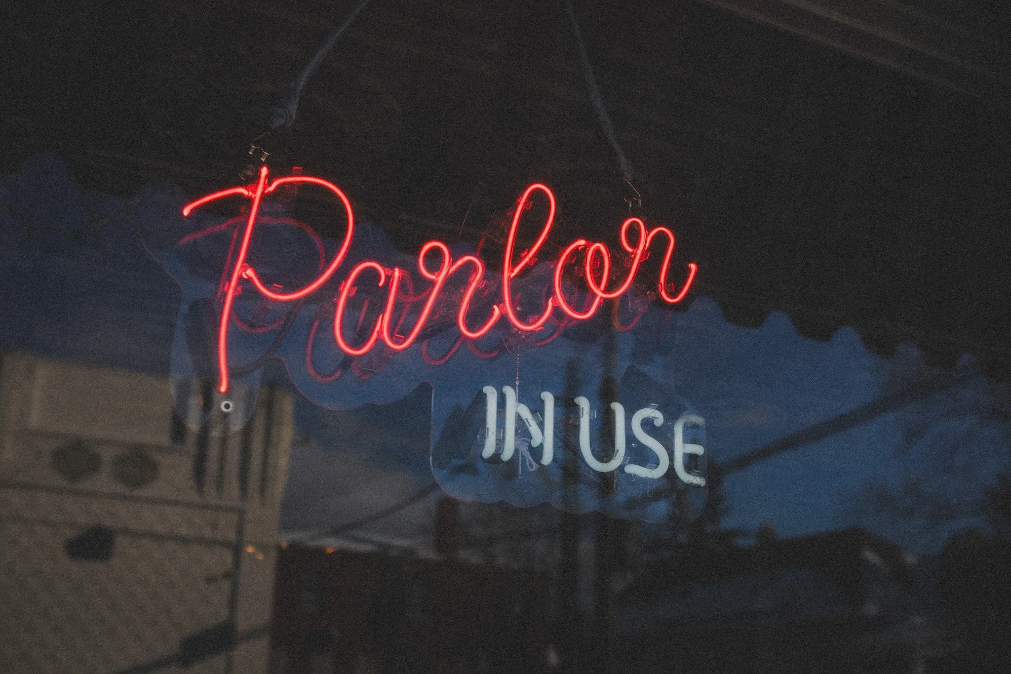 Neon sign with the words "Parlor IN USE" in red and white, hanging outdoors against a dark evening sky.