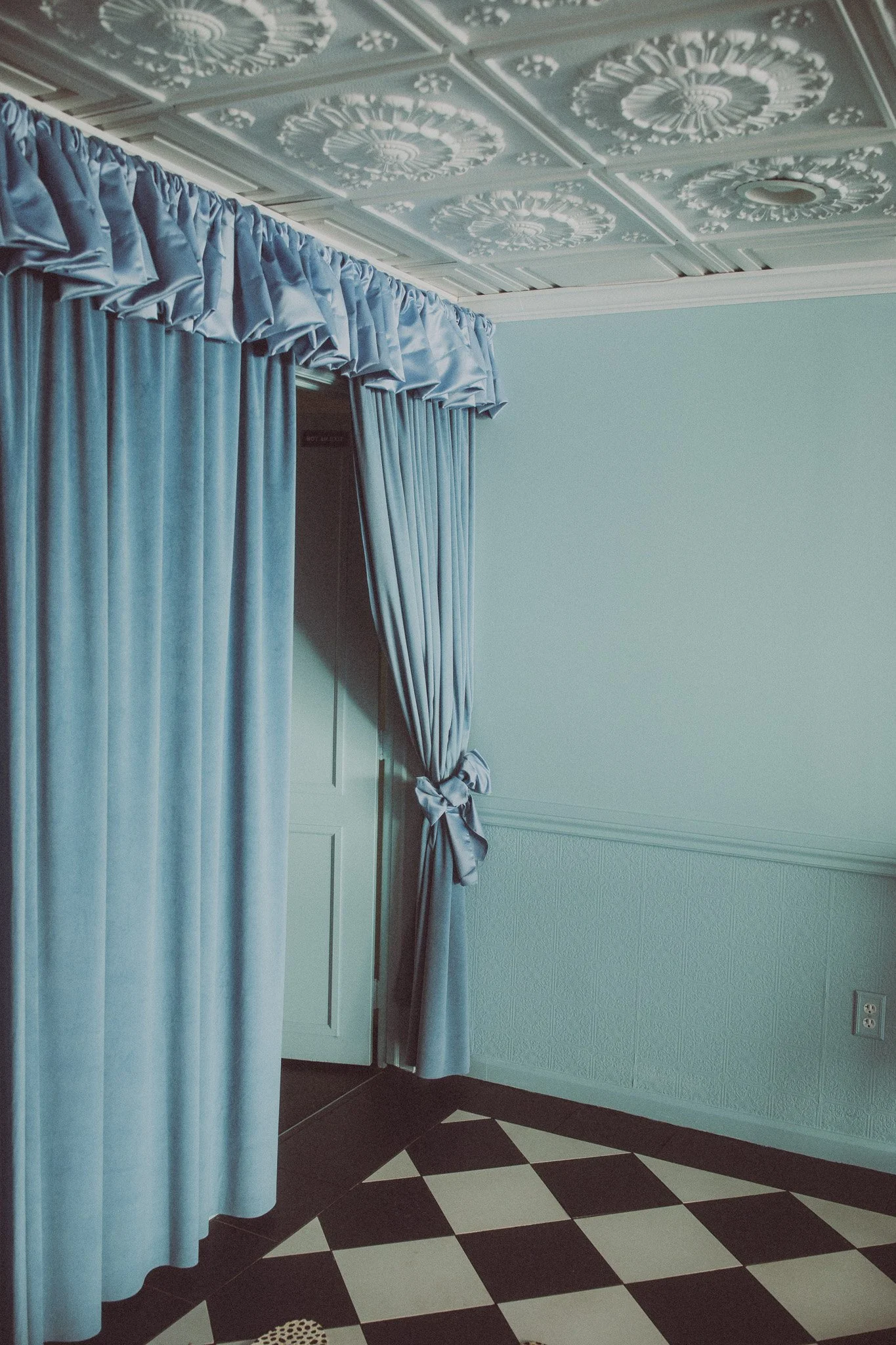 Blue curtains in a room with decorative ceiling panels and black-and-white checkered floor.