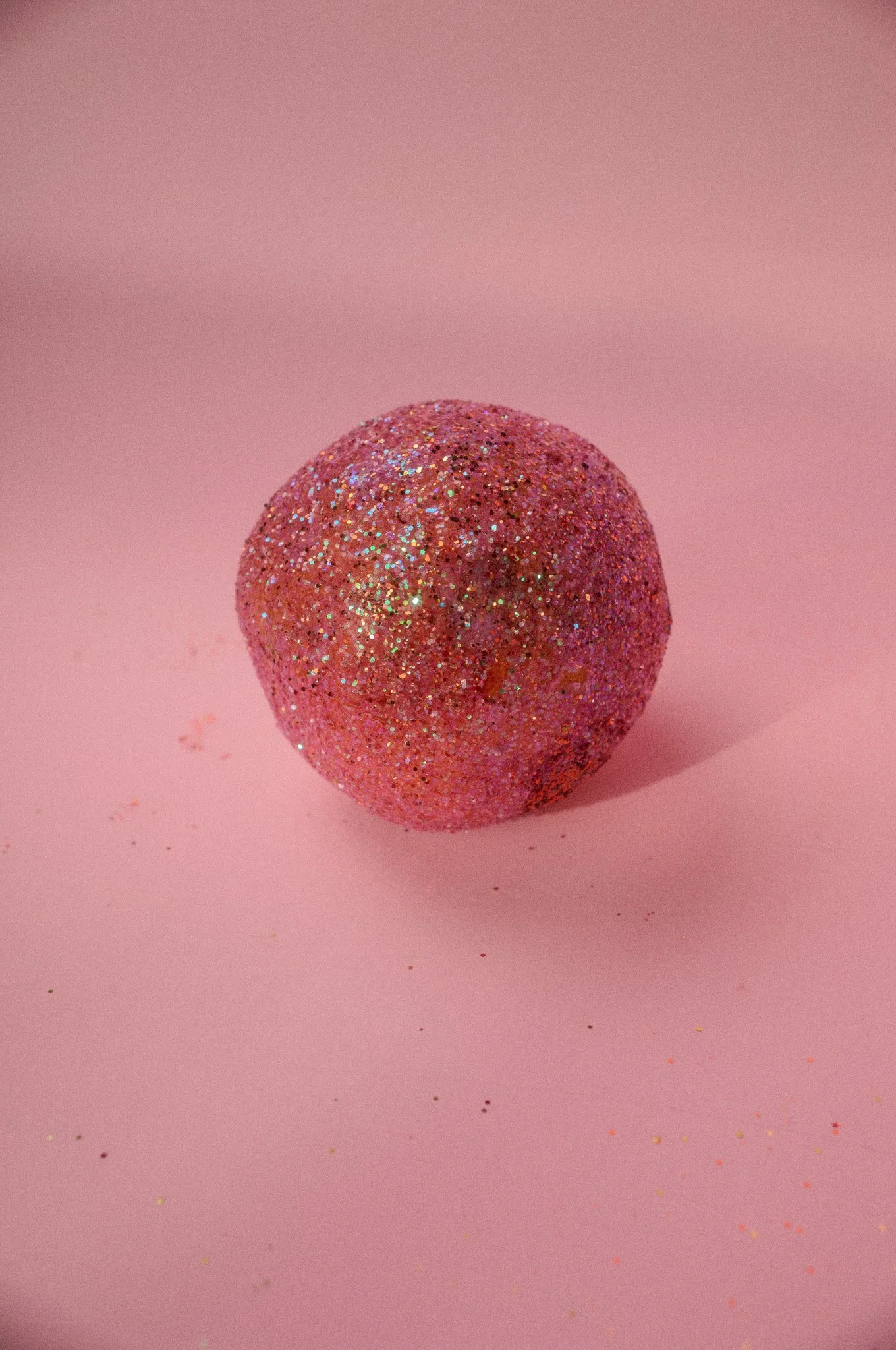 A pink glittery ball on a pink background.