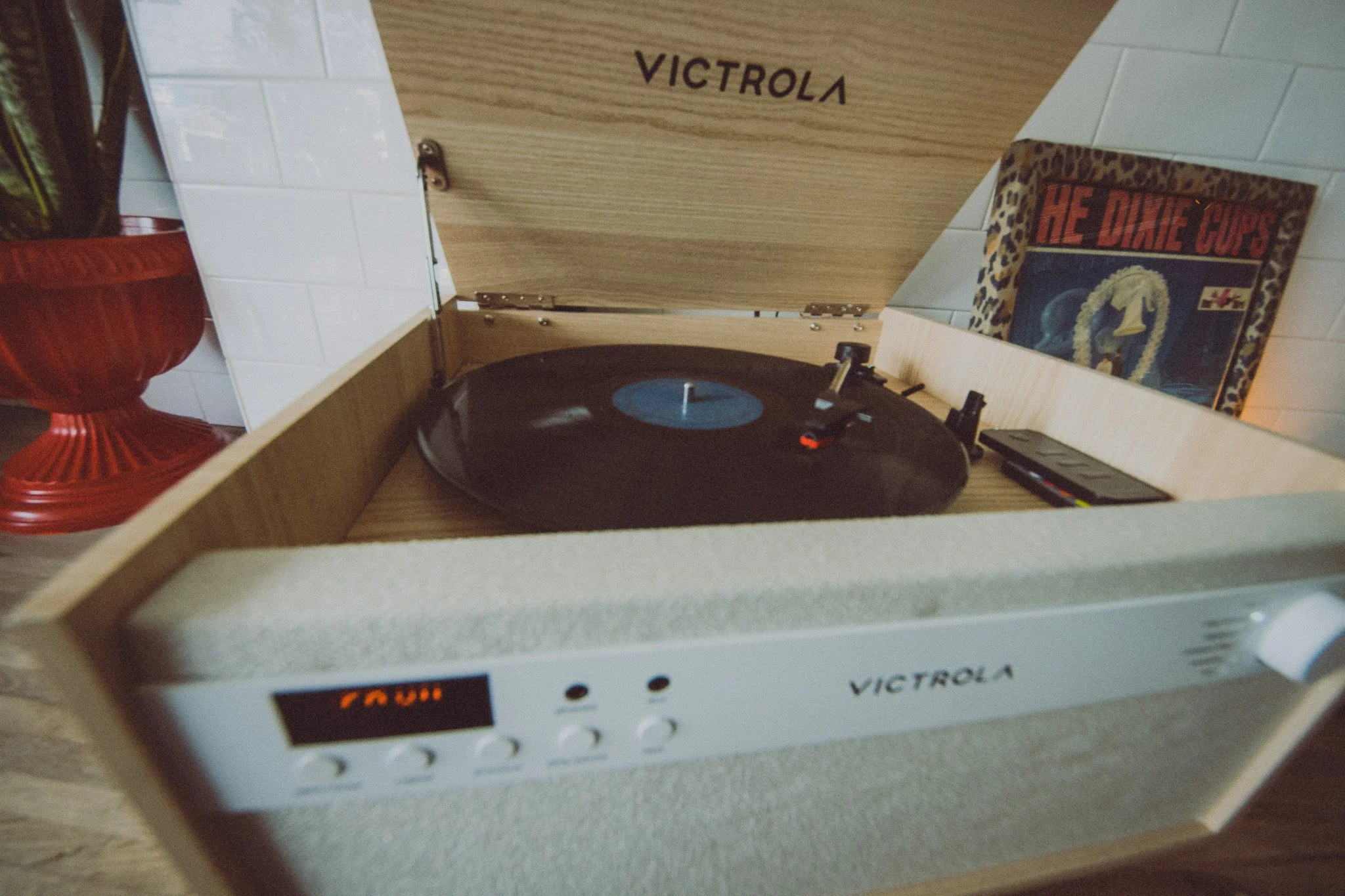 A vintage Victrola record player with a vinyl record on it, positioned inside a wooden cabinet with the lid open, on a counter or table.