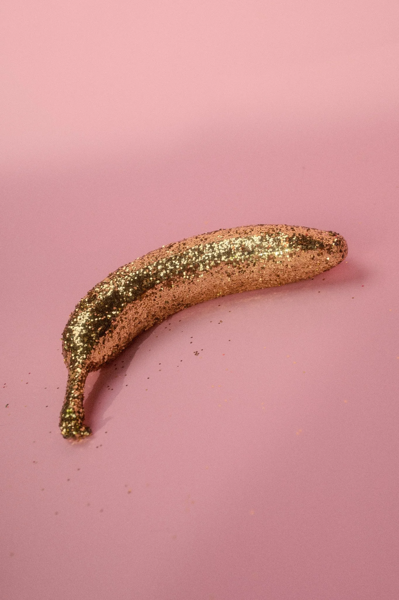 A curved object covered in gold and silver glitter on a pink background.