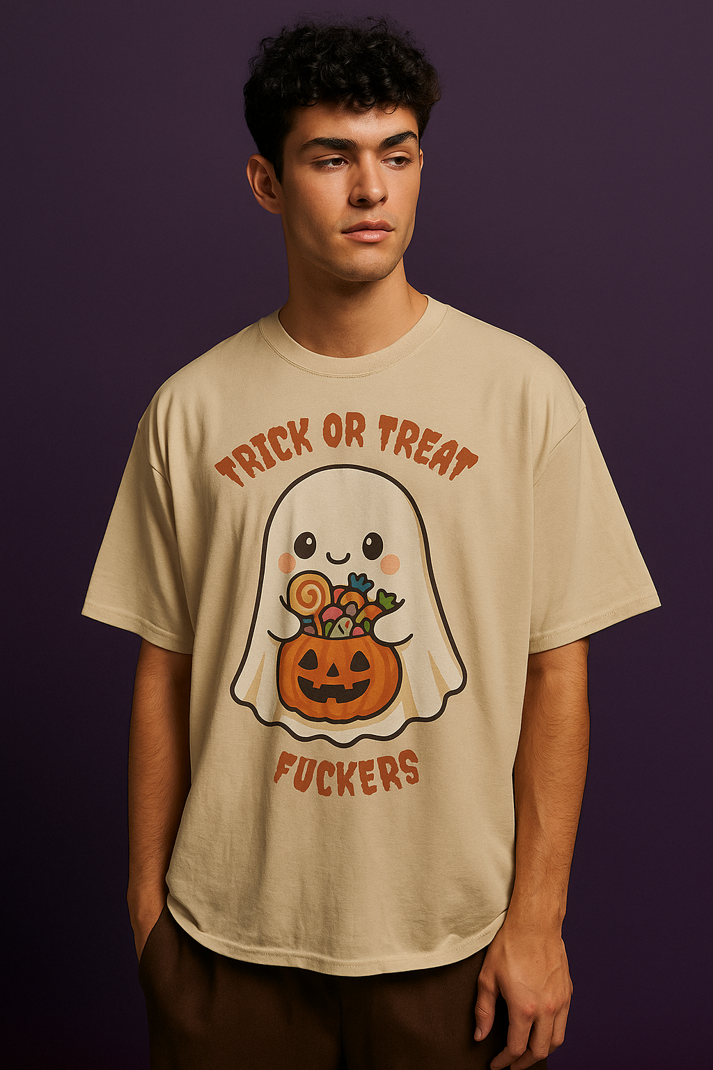 A young man wearing a beige Halloween-themed T-shirt with a cute ghost holding a jack-o'-lantern basket filled with candy, and the phrase "Trick or Treat Fuckers."