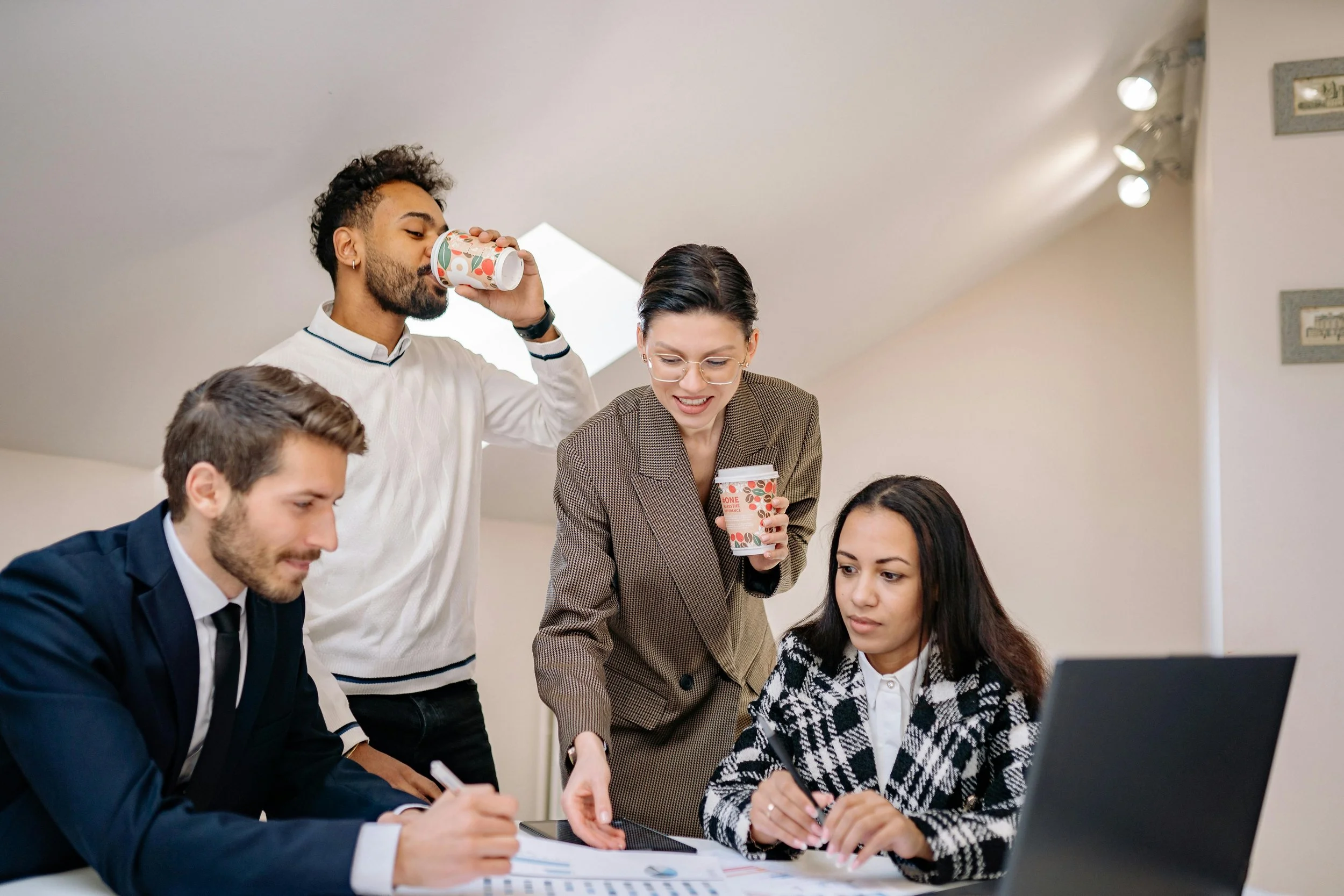 A modern building with large glass windows and stone walls is situated on a grassy hillside in front of snow-capped mountains under a cloudy sky.