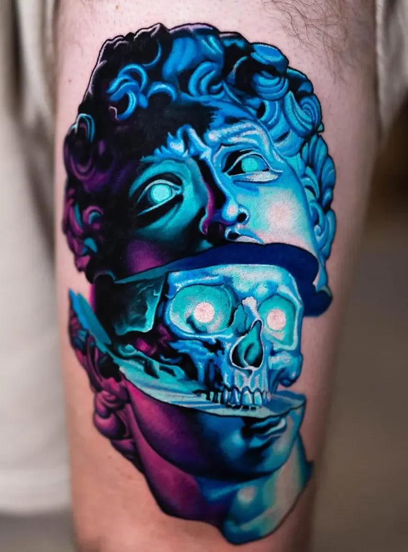 Tattoo of a classical statue with a skull, using vibrant blue, purple, and pink colors.