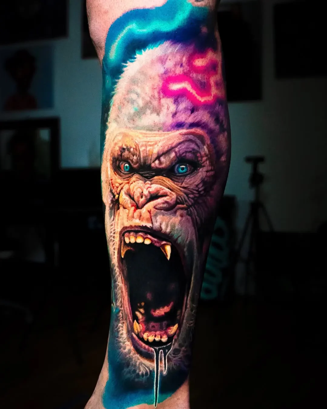 Colorful tattoo of an angry gorilla with piercing blue eyes, bared teeth, and open mouth on a person's arm.