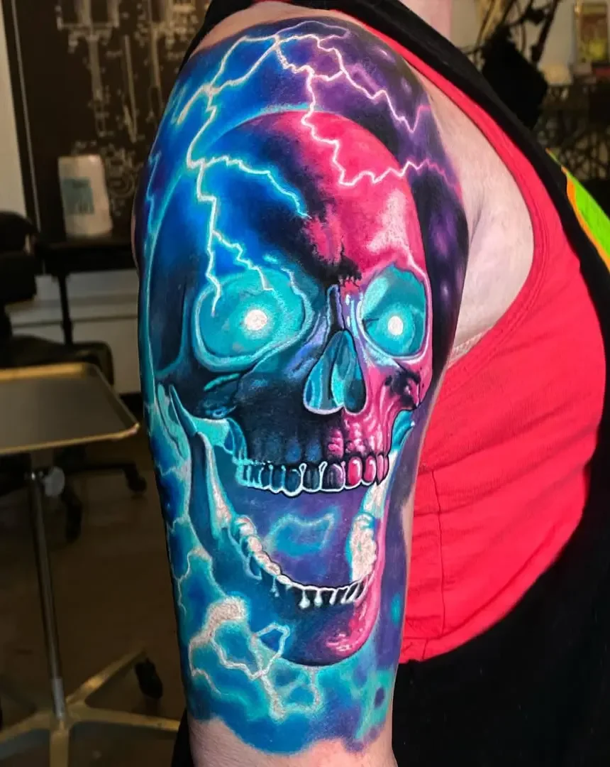 Colorful tattoo of a skull with lightning bolts and electric effects on person's upper arm.