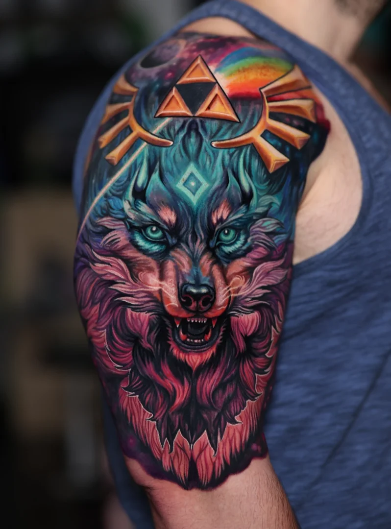 Colorful tattoo of a wolf's head with blue eyes, snarling, on a person's left shoulder and upper arm, with vibrant rainbow and cosmic background elements.