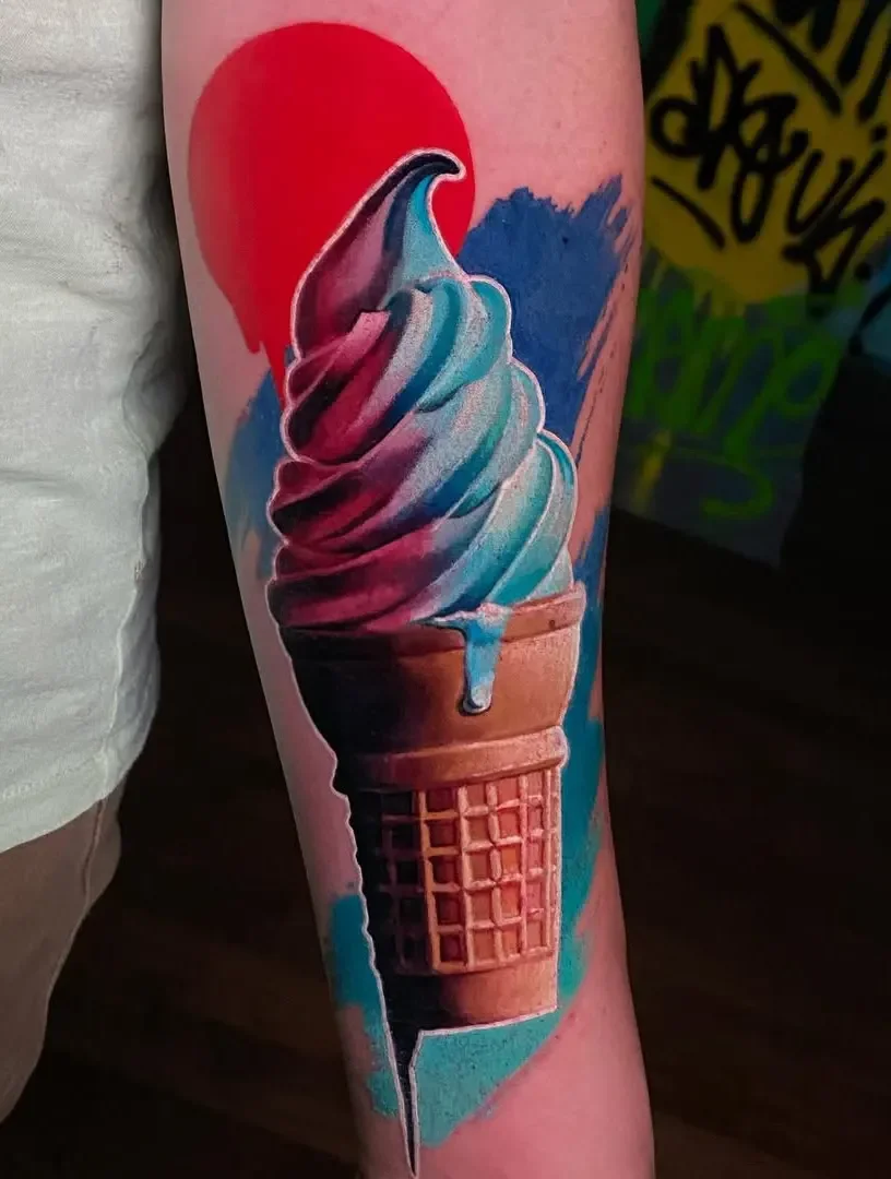 Colorful tattoo of an ice cream cone with a swirl of vanilla, blue, pink, and purple ice cream, with a red cherry on top, on a person's arm.