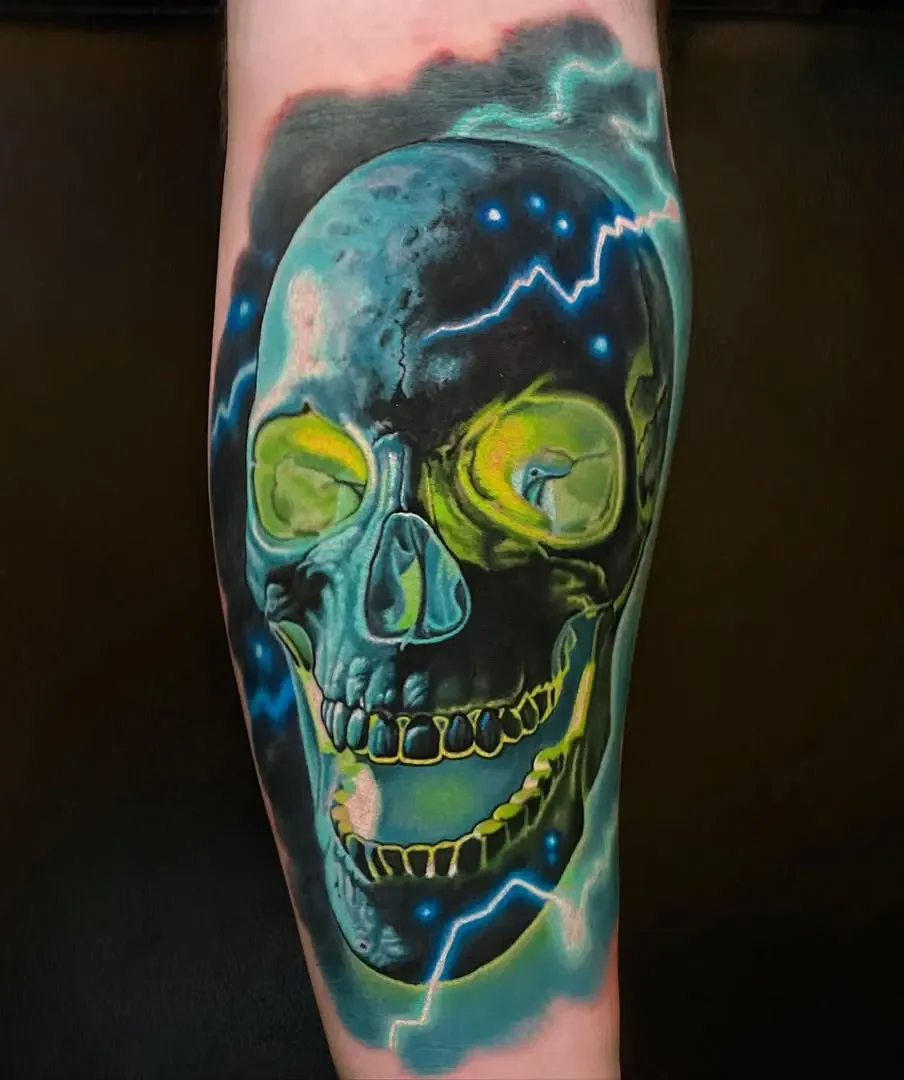 Tattoo of a colorful skull with lightning and cosmic background on person's leg.