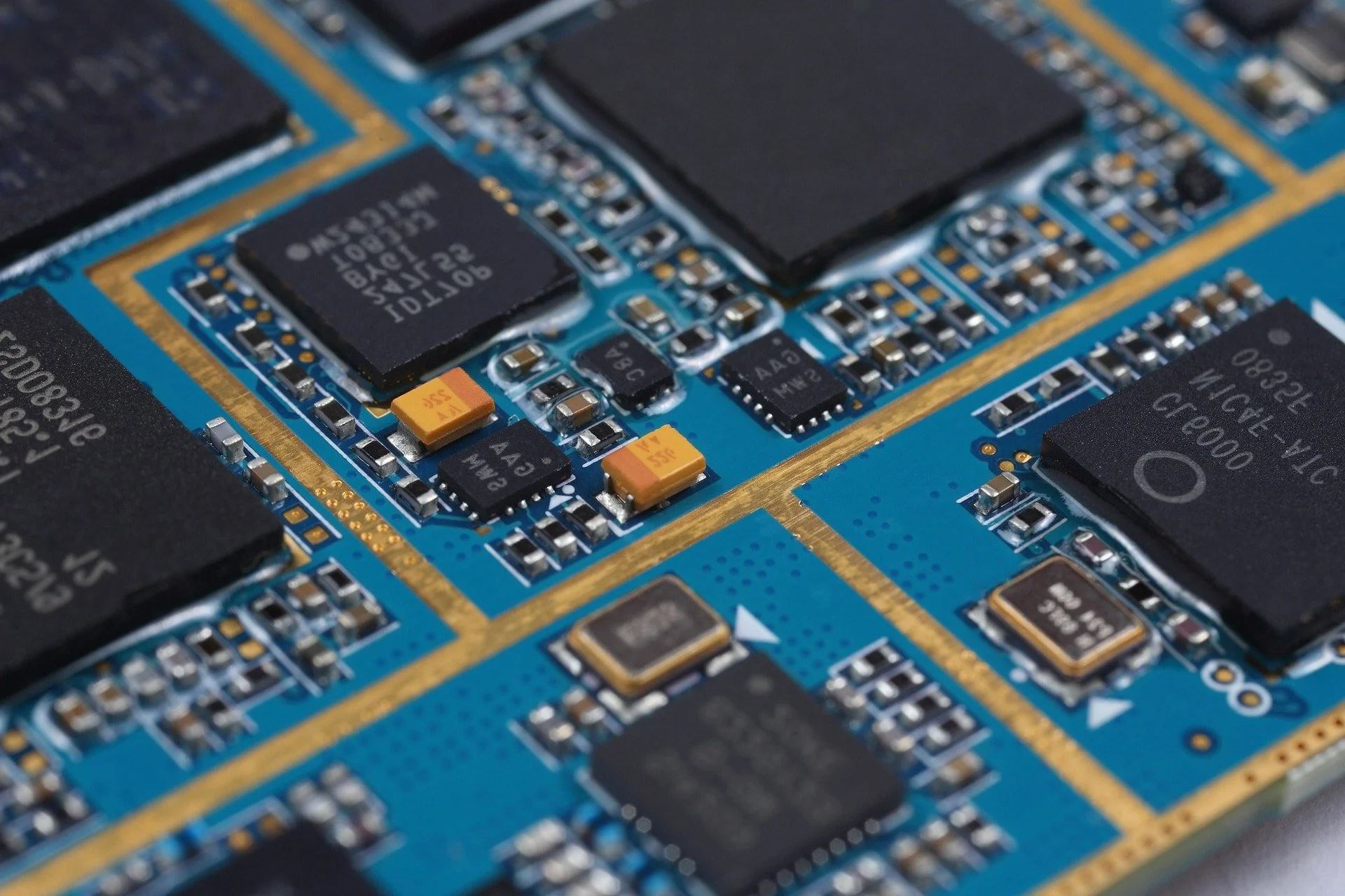 Close-up of a blue printed circuit board with various electronic components, including black chips, yellow capacitors, and small surface-mounted resistors.