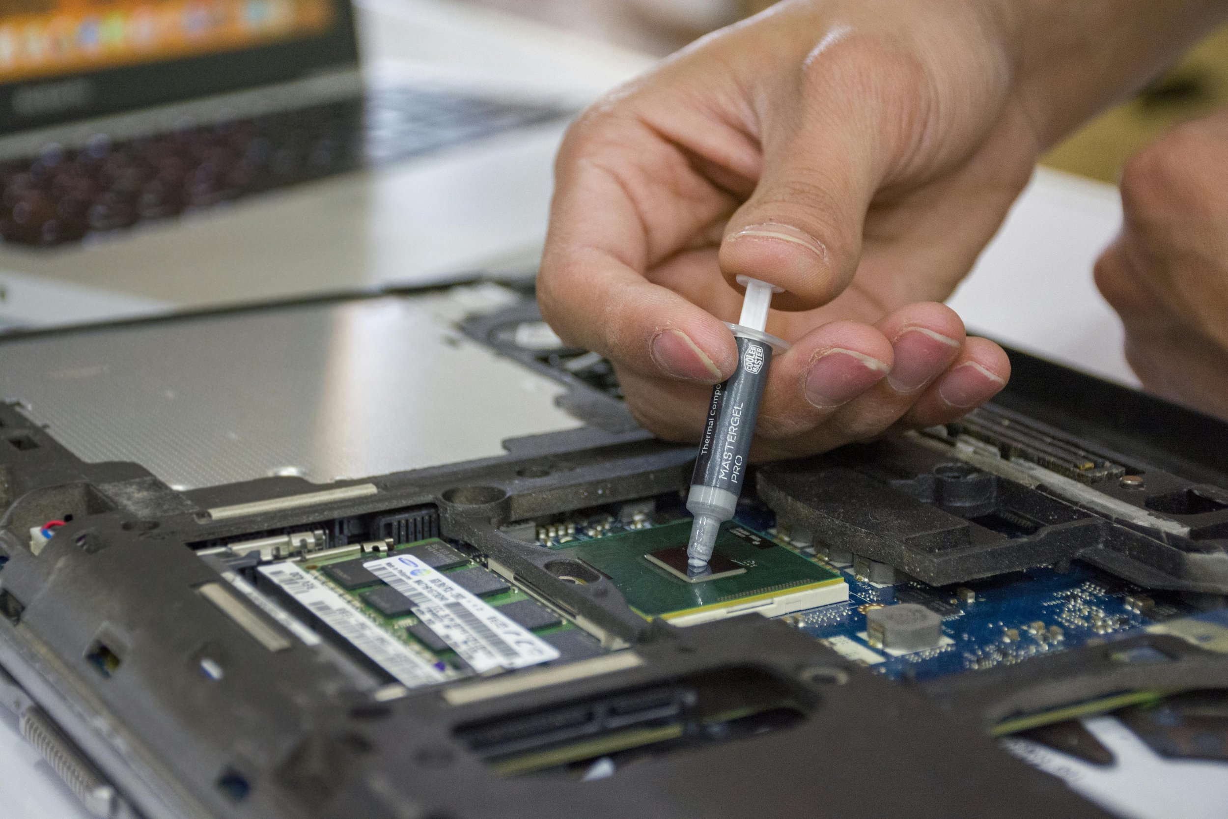 Close-up of a person replacing or installing a computer processor in a laptop, using thermal paste or adhesive on the CPU.
