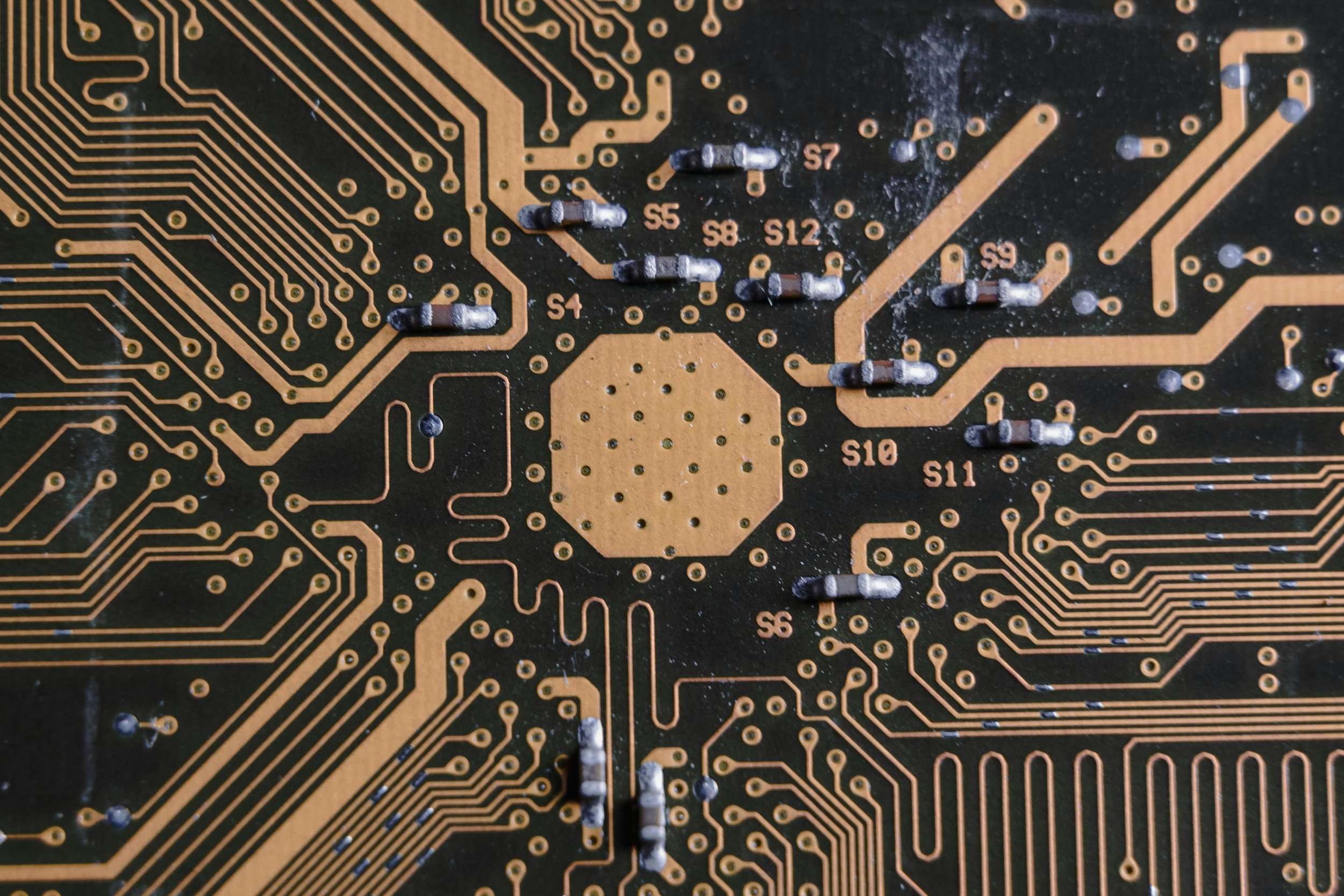 Close-up of a black printed circuit board with gold-colored traces and soldered components, including resistors labeled S4 to S12.