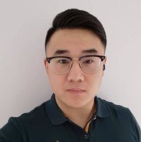 Portrait of a young man with black hair, glasses, and a serious expression, wearing a dark polo shirt, standing against a plain white background.