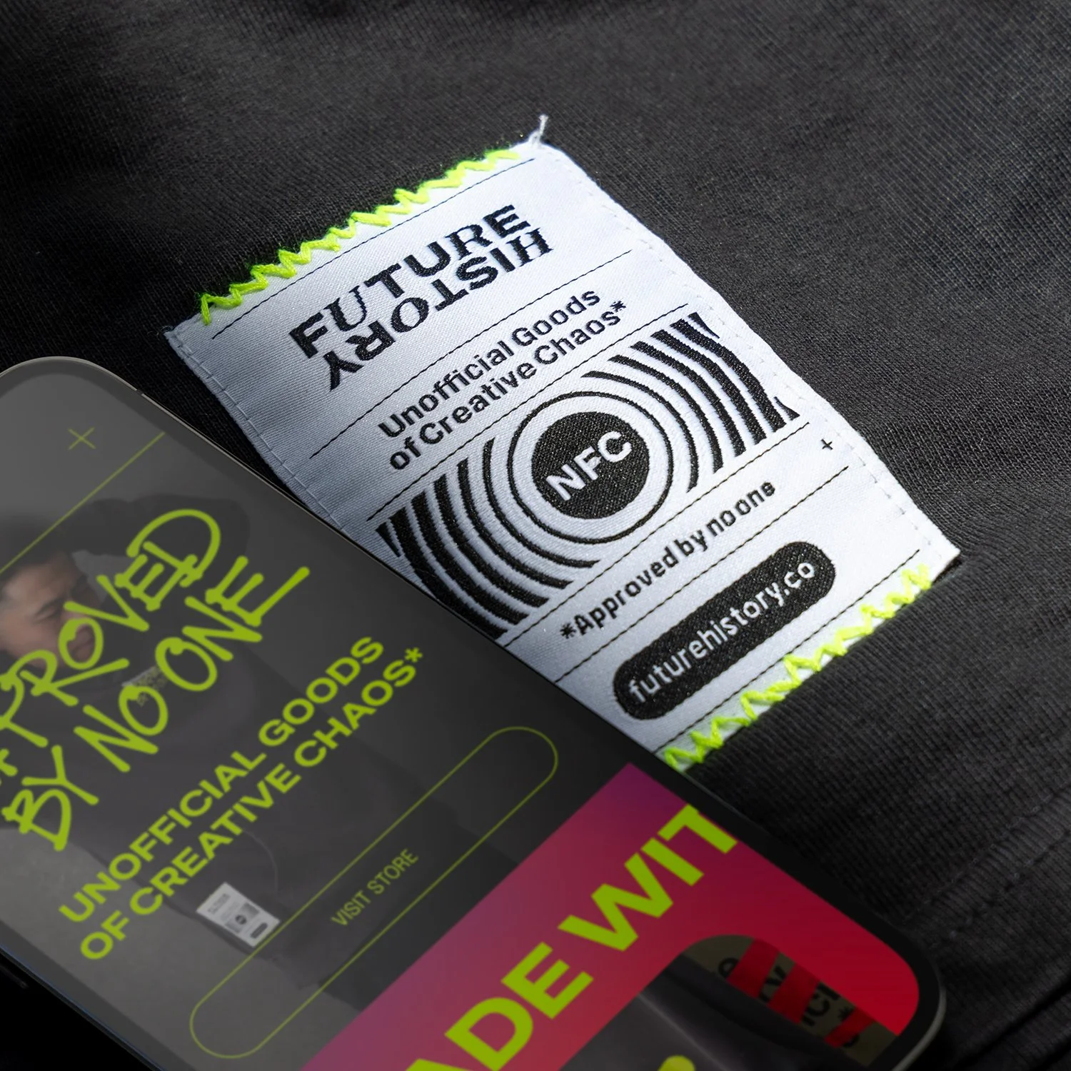 Close-up of a clothing tag with 'FUTURE SHIPPING' and 'Unauthorized Goods of Creative Chaos' printed on it, supported by neon green stitching, and a partially visible phone screen showing the same message.