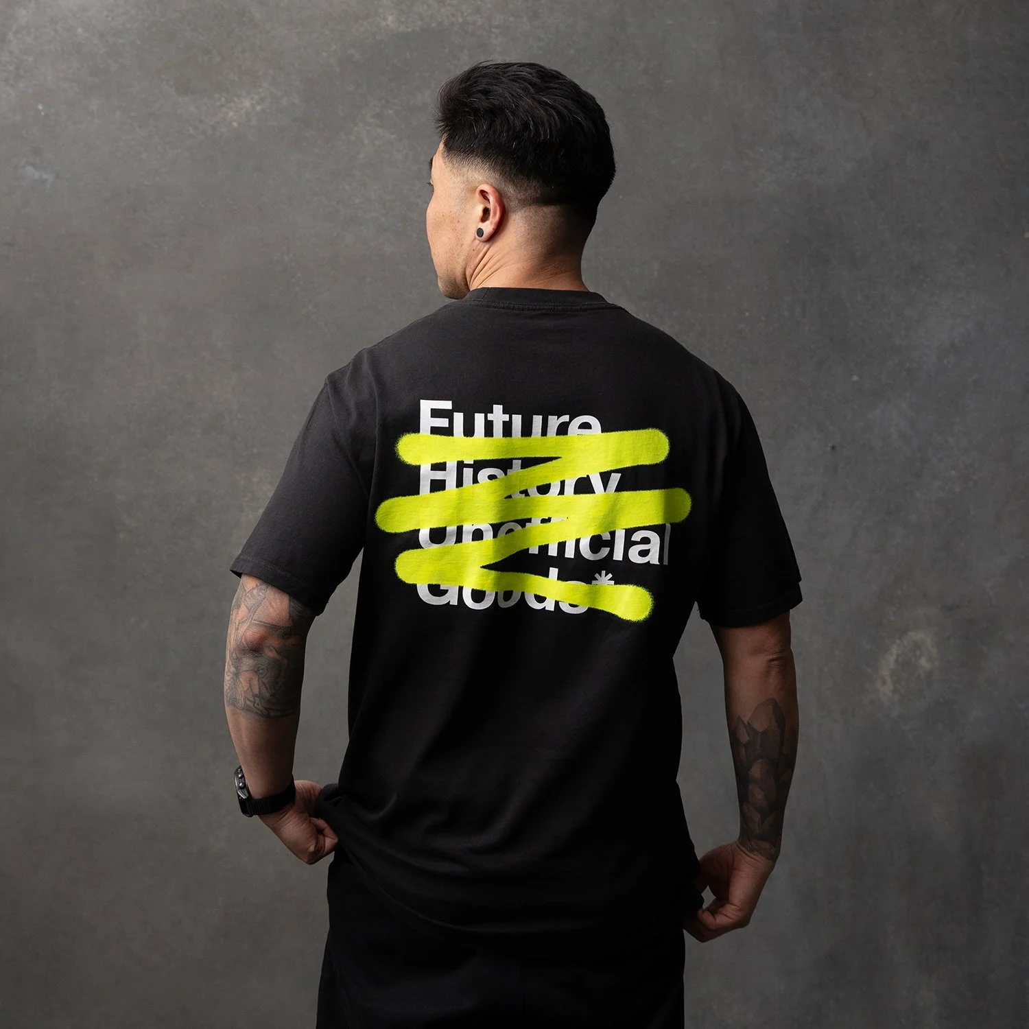 Back of a person wearing a black t-shirt with white text 'Future History Unethical Global' crossed out with yellow highlight.
