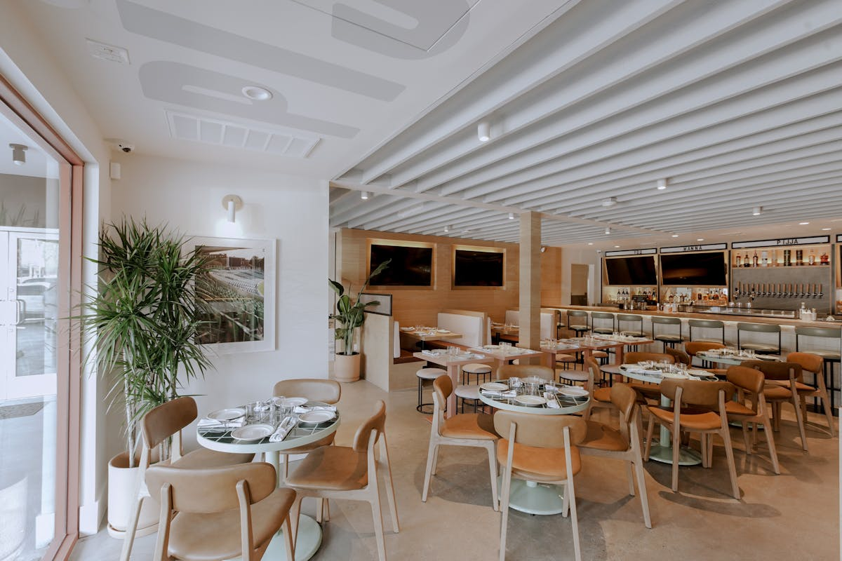 Empty restaurant interior with round tables, tan chairs, and a bar area.