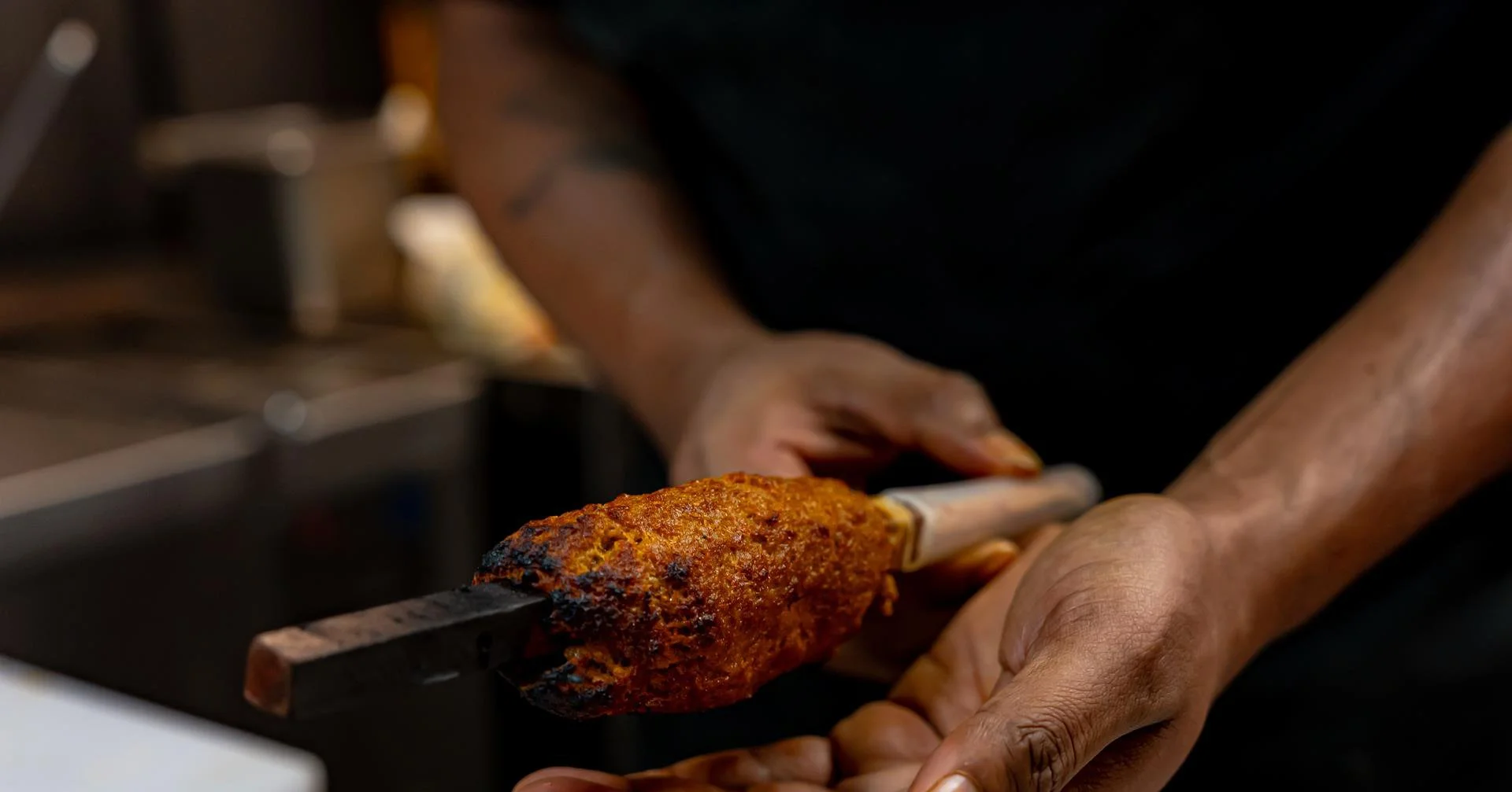 Close-up of a person holding a skewer with grilled meat.